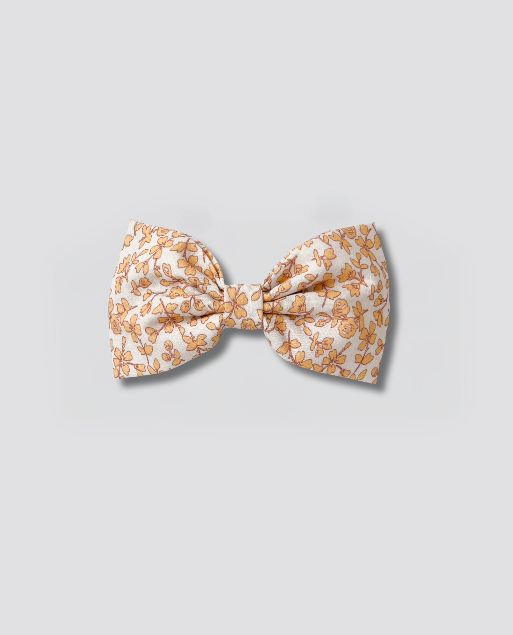 Soft fabric bow clip for girls with a delicate vintage-inspired floral pattern in warm tones, crafted with natural materials for sustainable, ethical children's fashion.