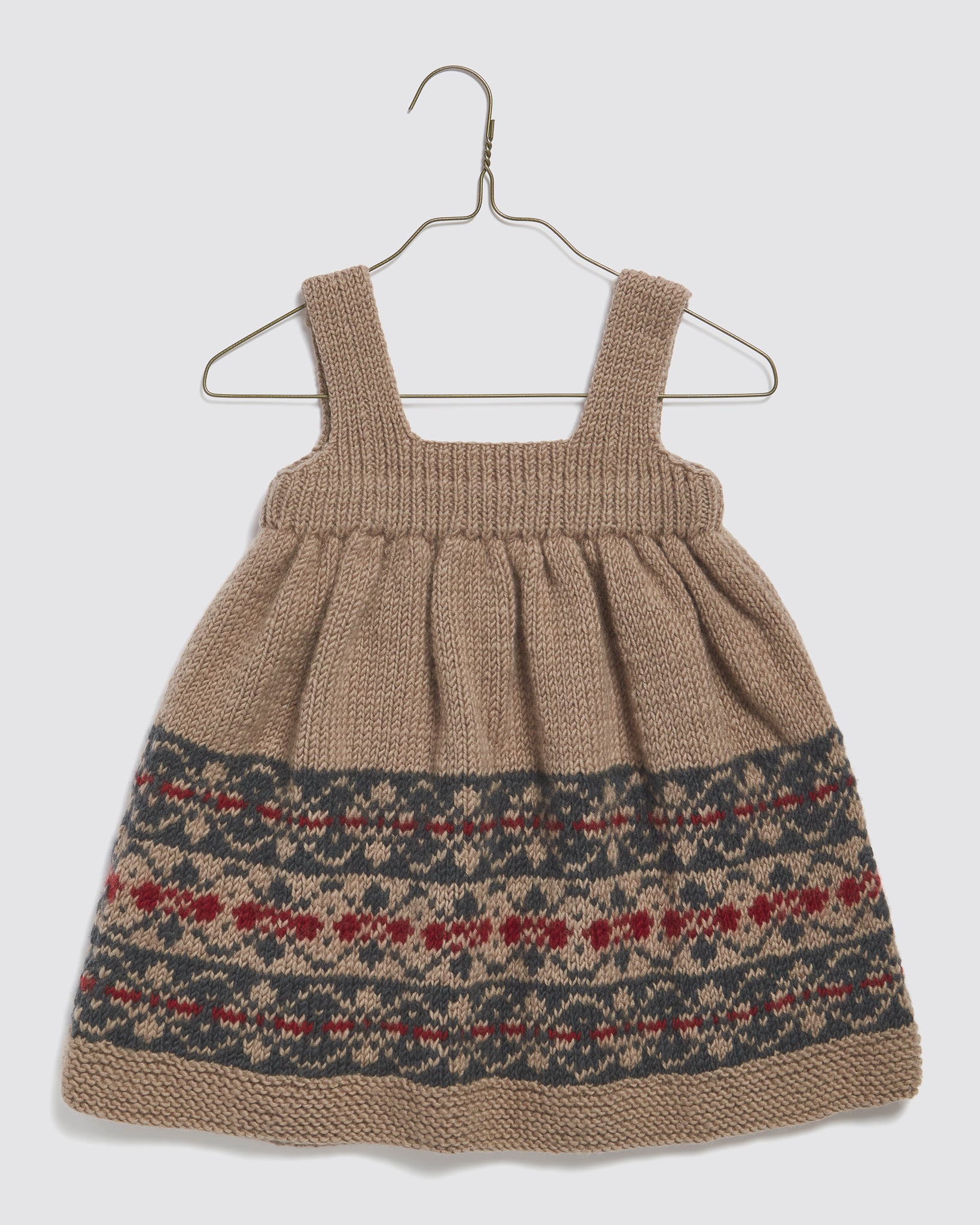 Hand-knitted pinafore dress for kids in beige merino wool featuring a vintage-style Fair Isle pattern in navy, blue, multicolor, and beige, ethically made with natural materials.