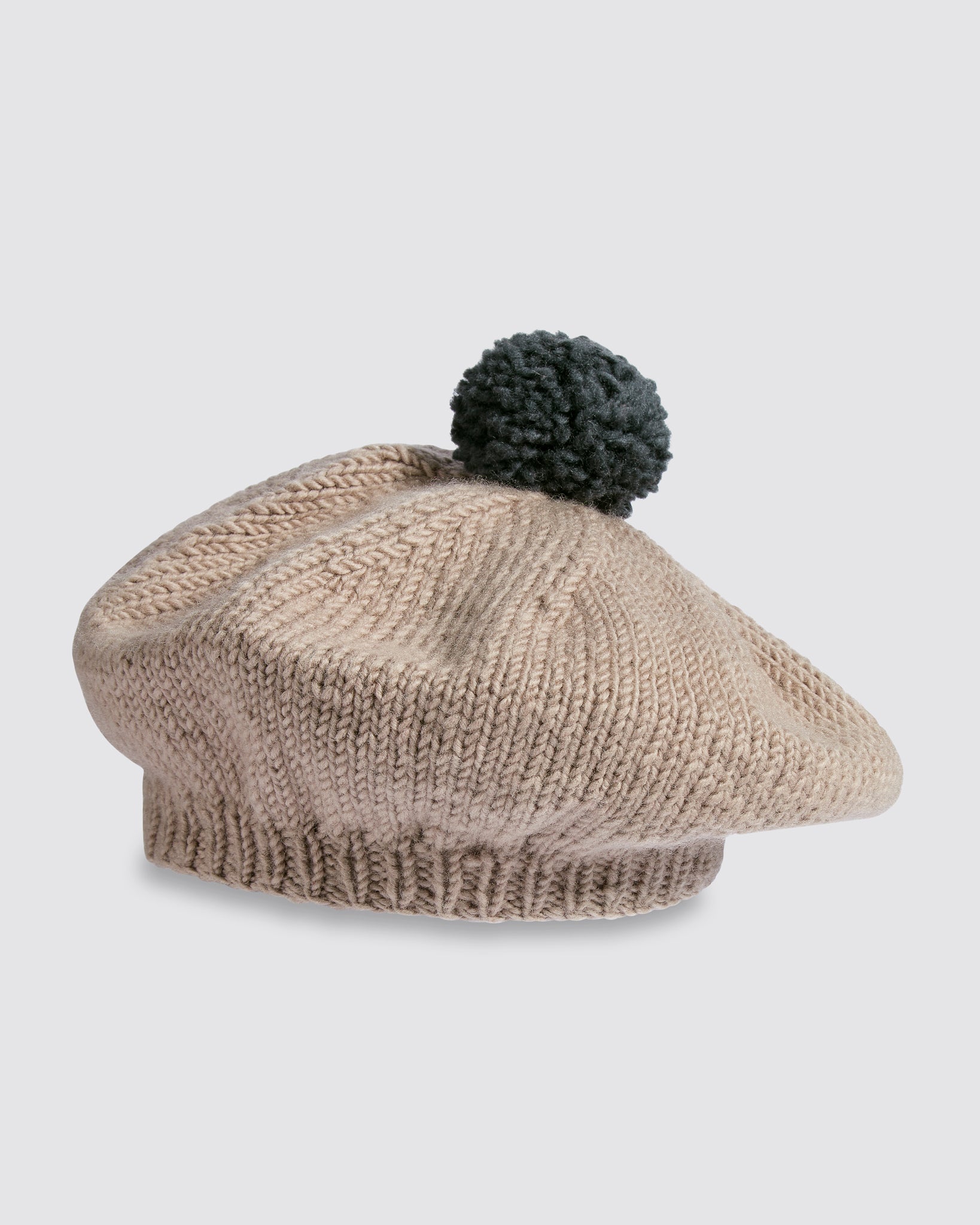 Hand-knitted kids beret made from soft merino wool in natural oat color with a vintage style and a black pom-pom, crafted sustainably with organic materials.
