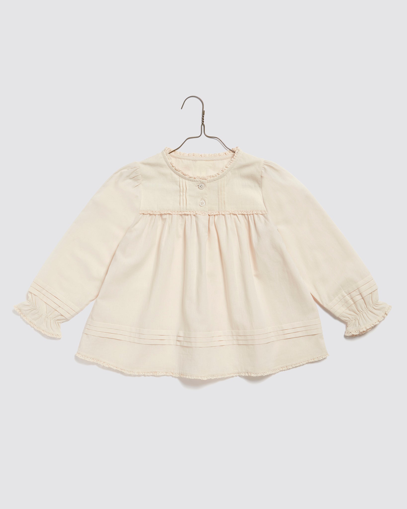 Soft pale cream long-sleeve blouse for girls made from organic natural cotton, featuring delicate vintage-inspired details and a gentle gathered design for comfort.