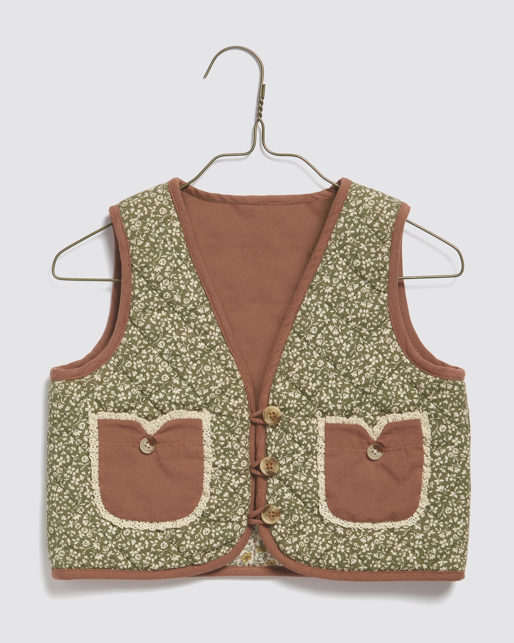 Green floral quilted waistcoat for kids made from organic cotton with brown trim and button details, reflecting vintage and sustainable children's clothing style.