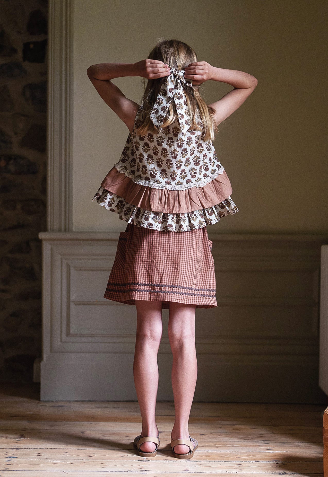 Young girl wearing vintage style girls blouse with floral and check patterns in pink and white, styled with a matching hair accessory, showcasing sustainable organic children's clothing.