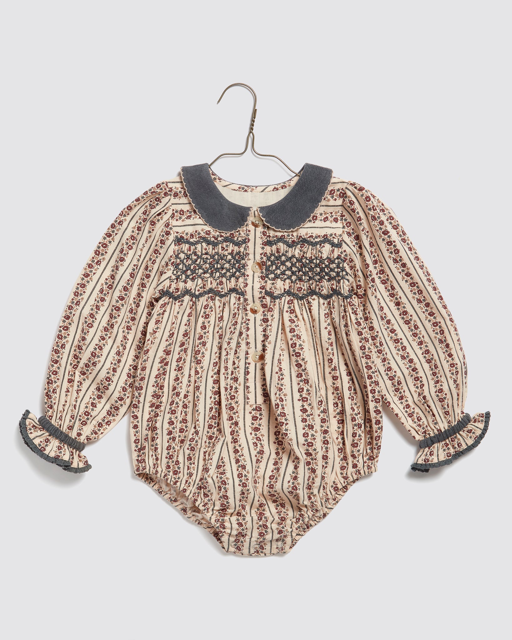 Vintage style girls romper made from organic cotton featuring long sleeves, a navy peter pan collar, smocked floral detailing, and striped floral pattern.