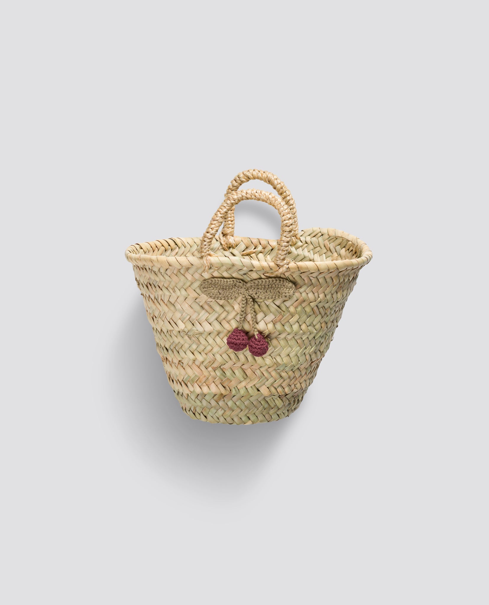 Small natural woven market basket with crochet cherry decoration, crafted from sustainable materials for a charming, vintage-inspired look.
