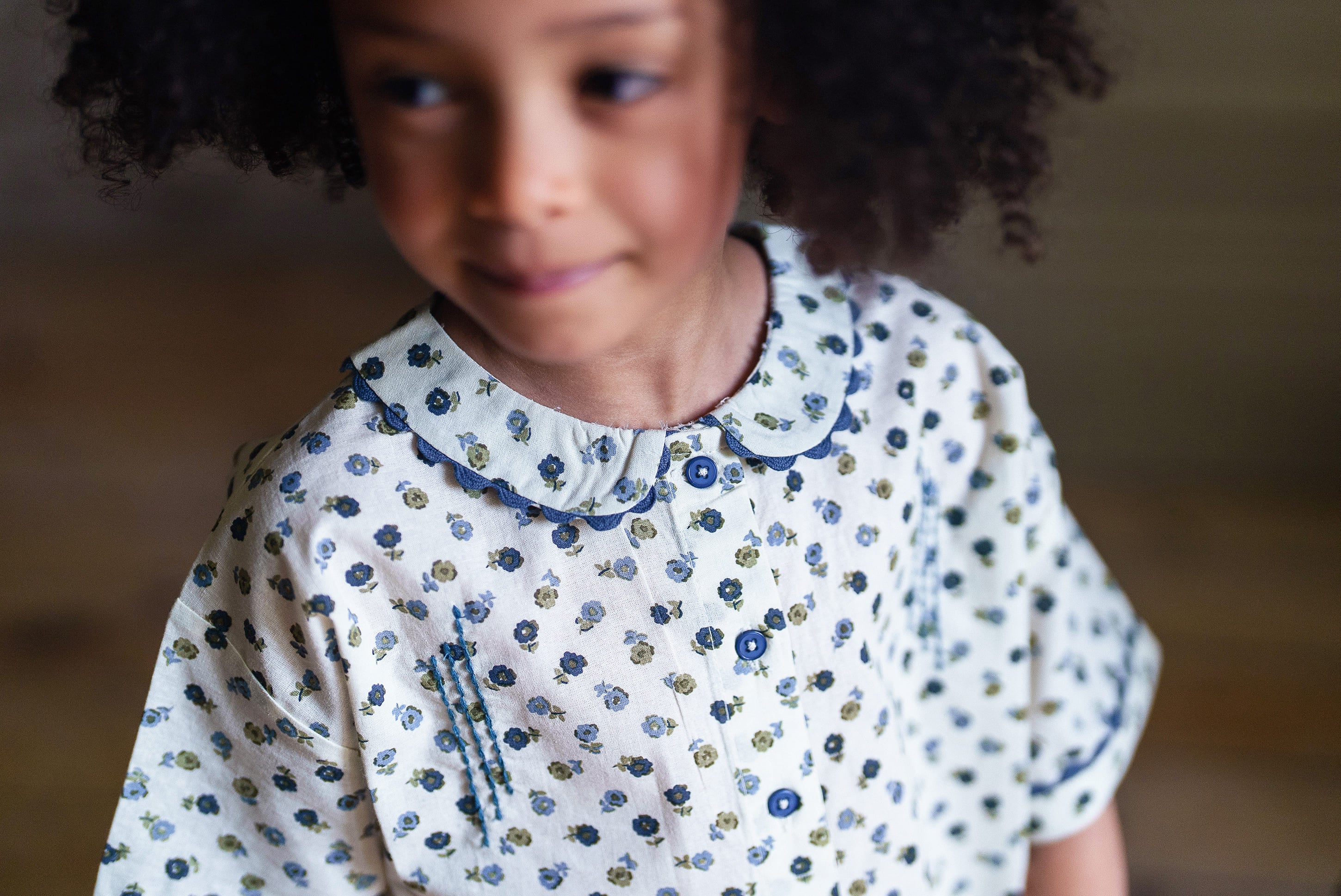 Young girl wearing a vintage-style cotton blouse with a delicate blue floral pattern, made from organic materials, reflecting sustainable and ethical children's clothing.