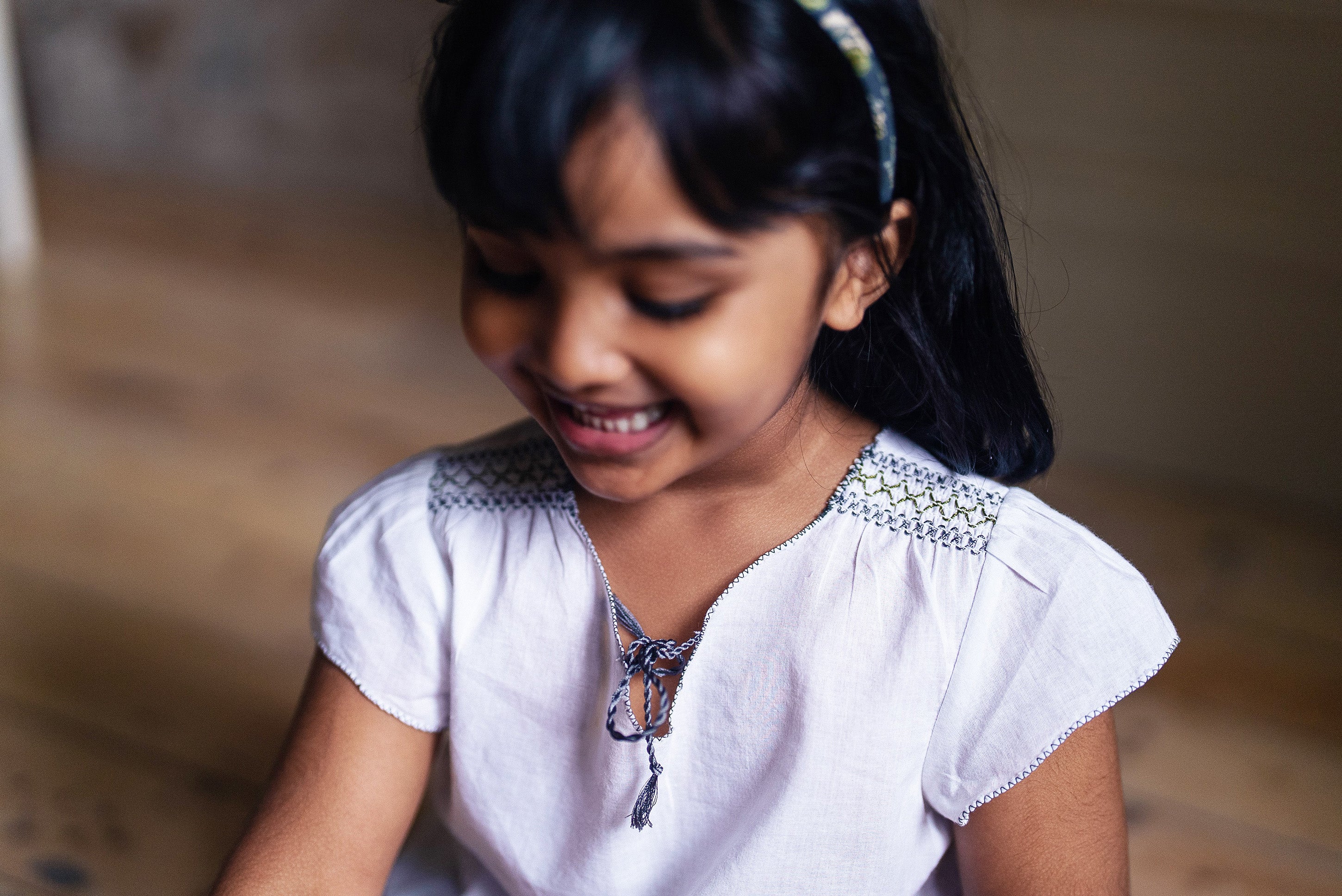 Young girl smiling wearing an off-white organic cotton blouse with delicate vintage-inspired embroidery, highlighting natural and sustainable children’s clothing.