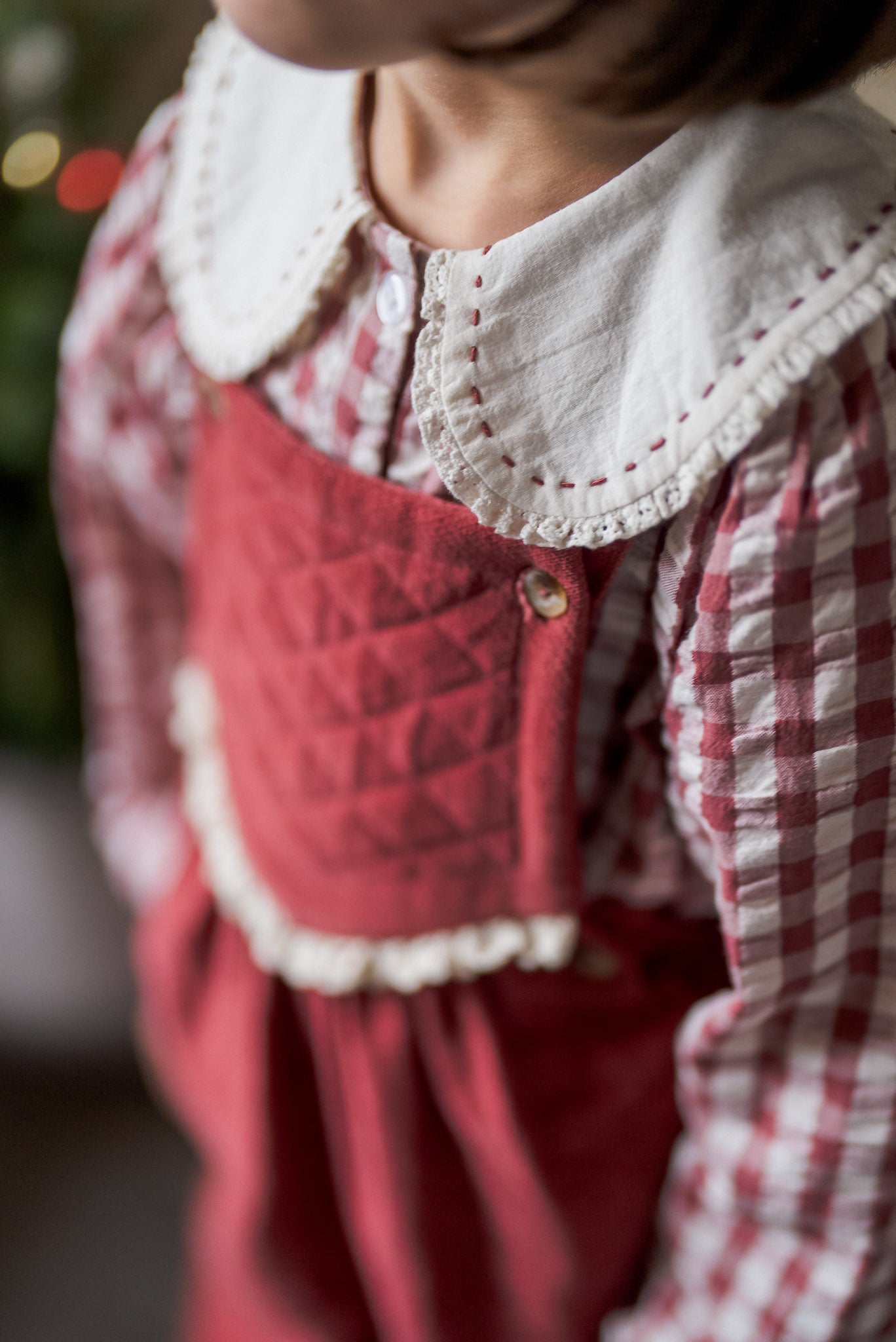 Close-up of a child wearing a white cotton blouse with a scalloped collar over a red and white checkered seersucker gingham fabric, featuring vintage-inspired sustainable kids clothing.