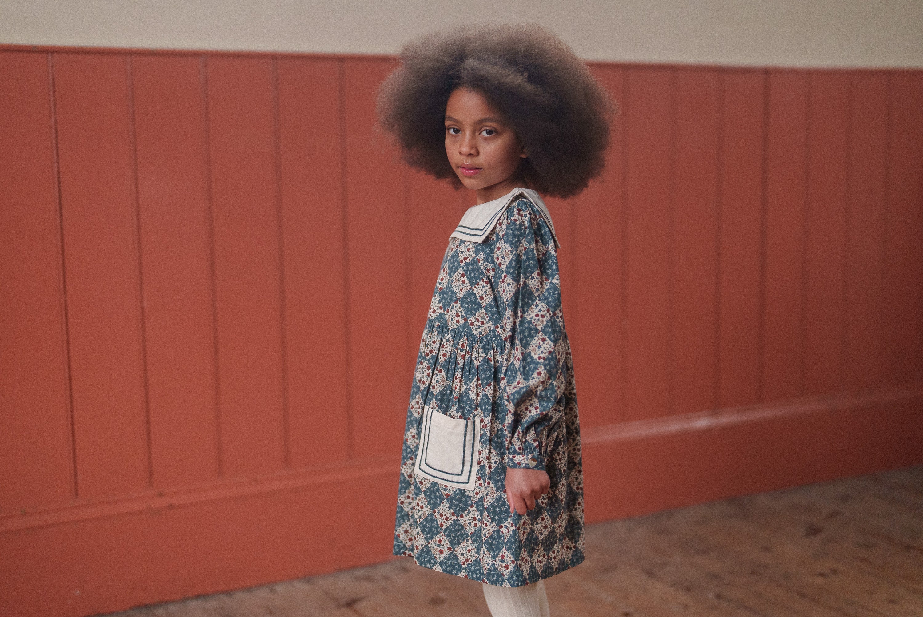 Young girl wearing a navy floral organic cotton vintage-style dress with a sailor collar, showcasing sustainable and ethically made children’s clothing.