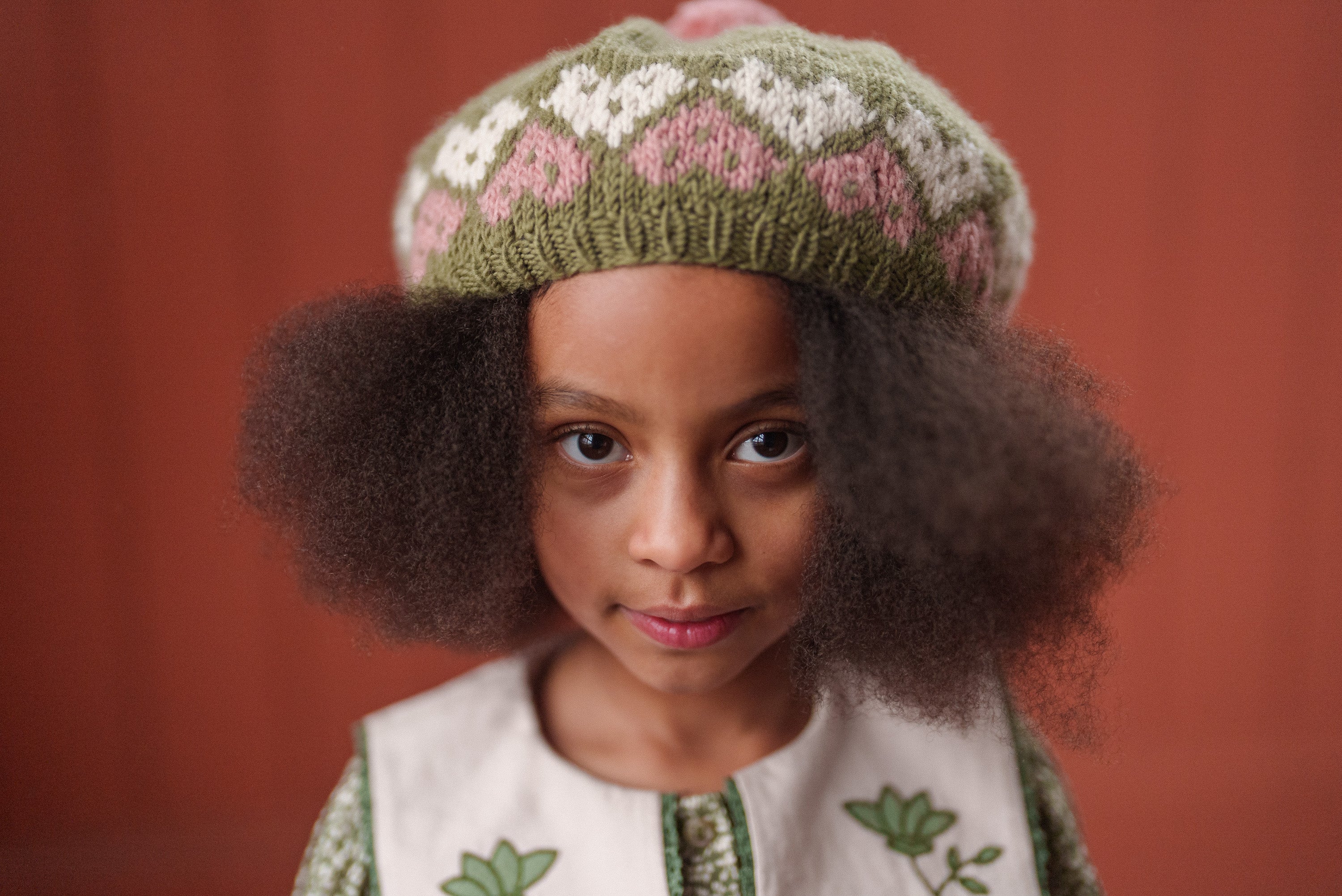 Close-up of a young girl wearing a vintage-style organic cotton dress with floral embroidery and a knitted green beret, showcasing sustainable children's clothing.