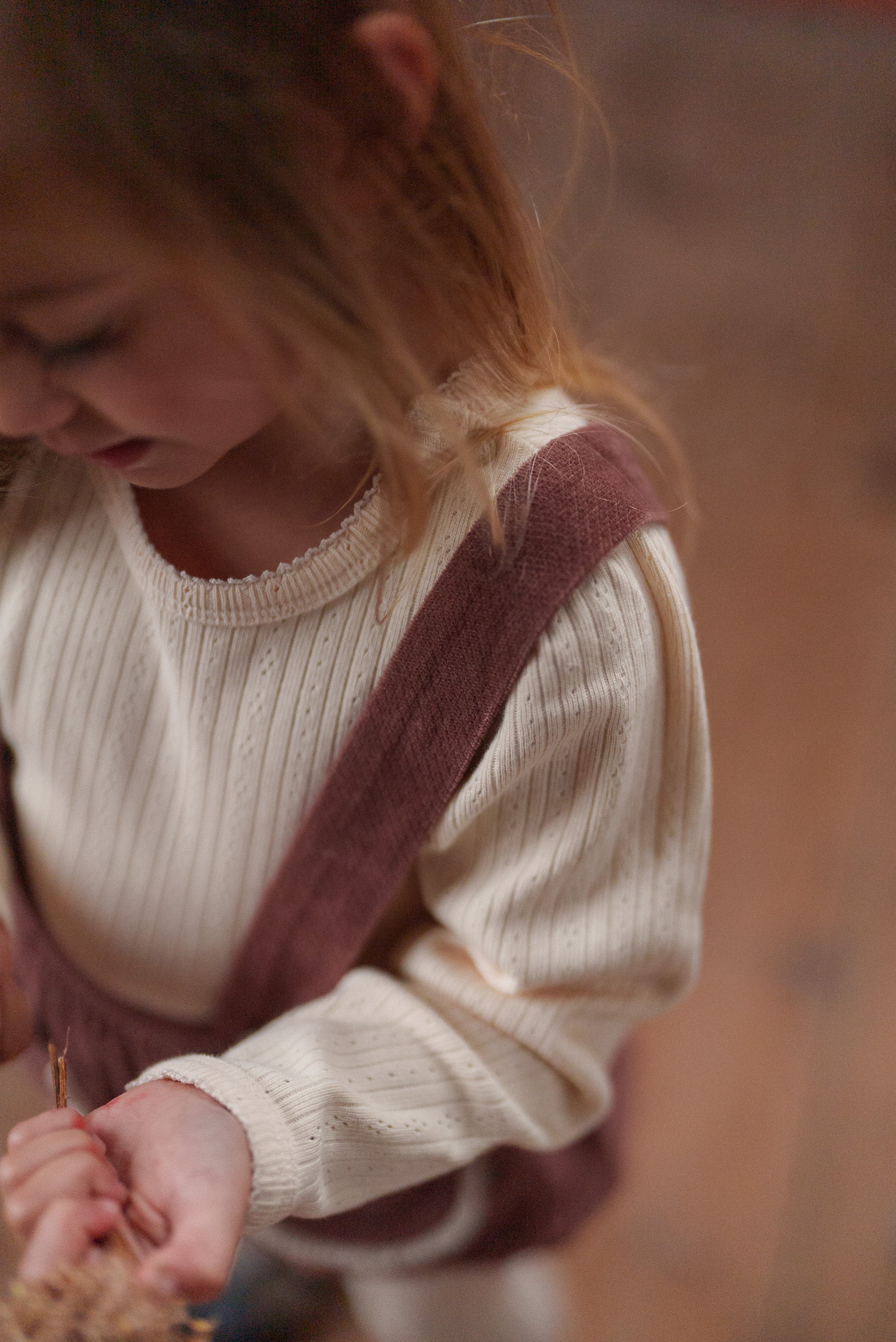 Close-up of a toddler wearing a cream organic cotton top with delicate eyelet details and a brown velvet romper, showcasing sustainable vintage style children's clothing.