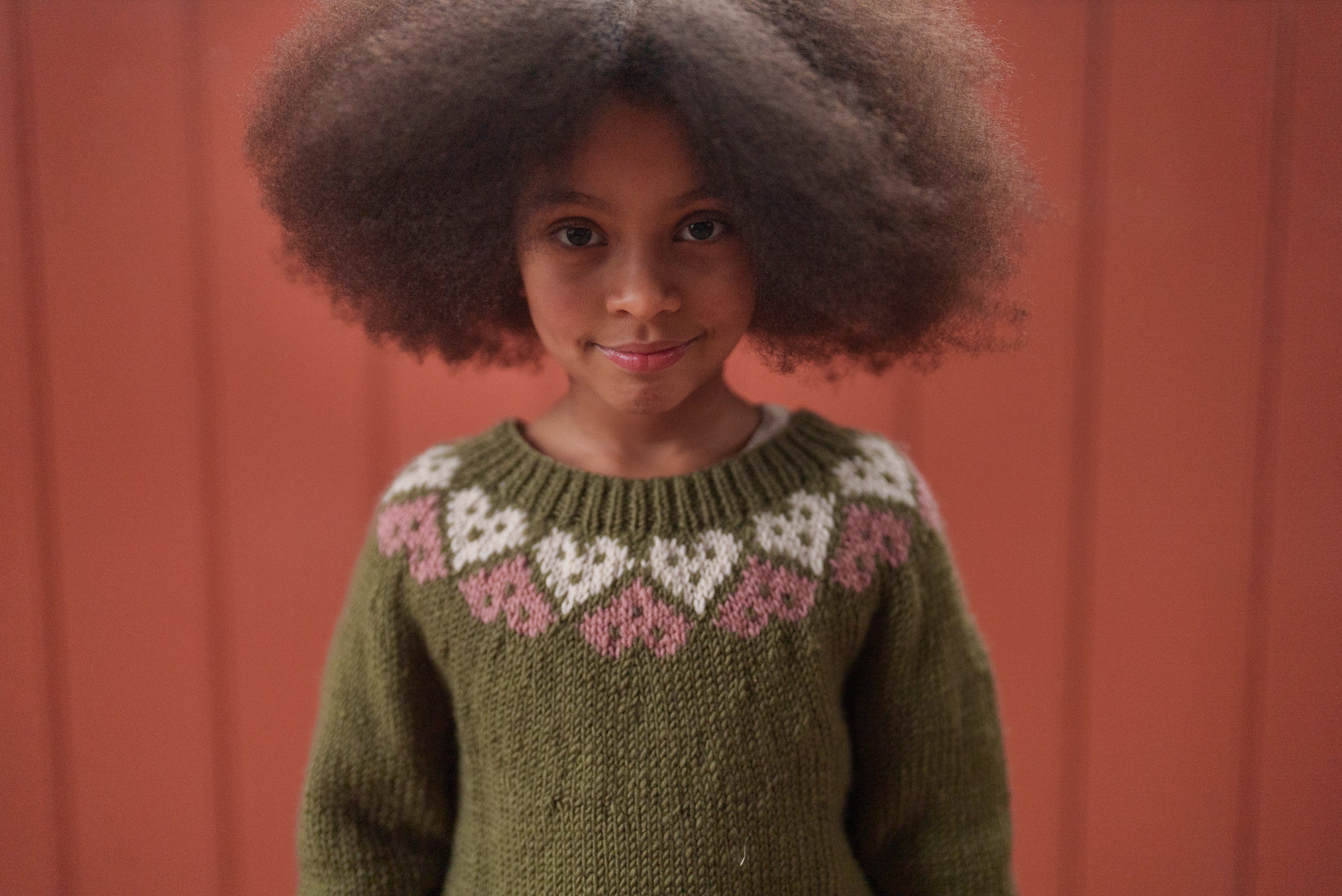 Young girl wearing a multicolor hand-knitted jumper made from soft merino wool, featuring heart patterns in vintage style, perfect ethical kids clothing.