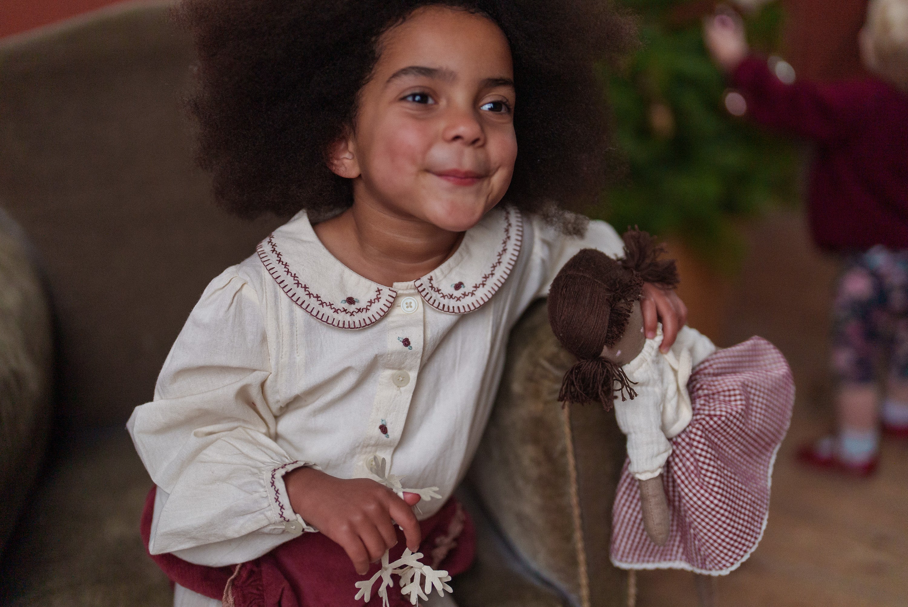 Young girl wearing vintage style children's clothing made from natural cotton and velvet, holding a soft doll, reflecting ethical and sustainable fashion for childhood.