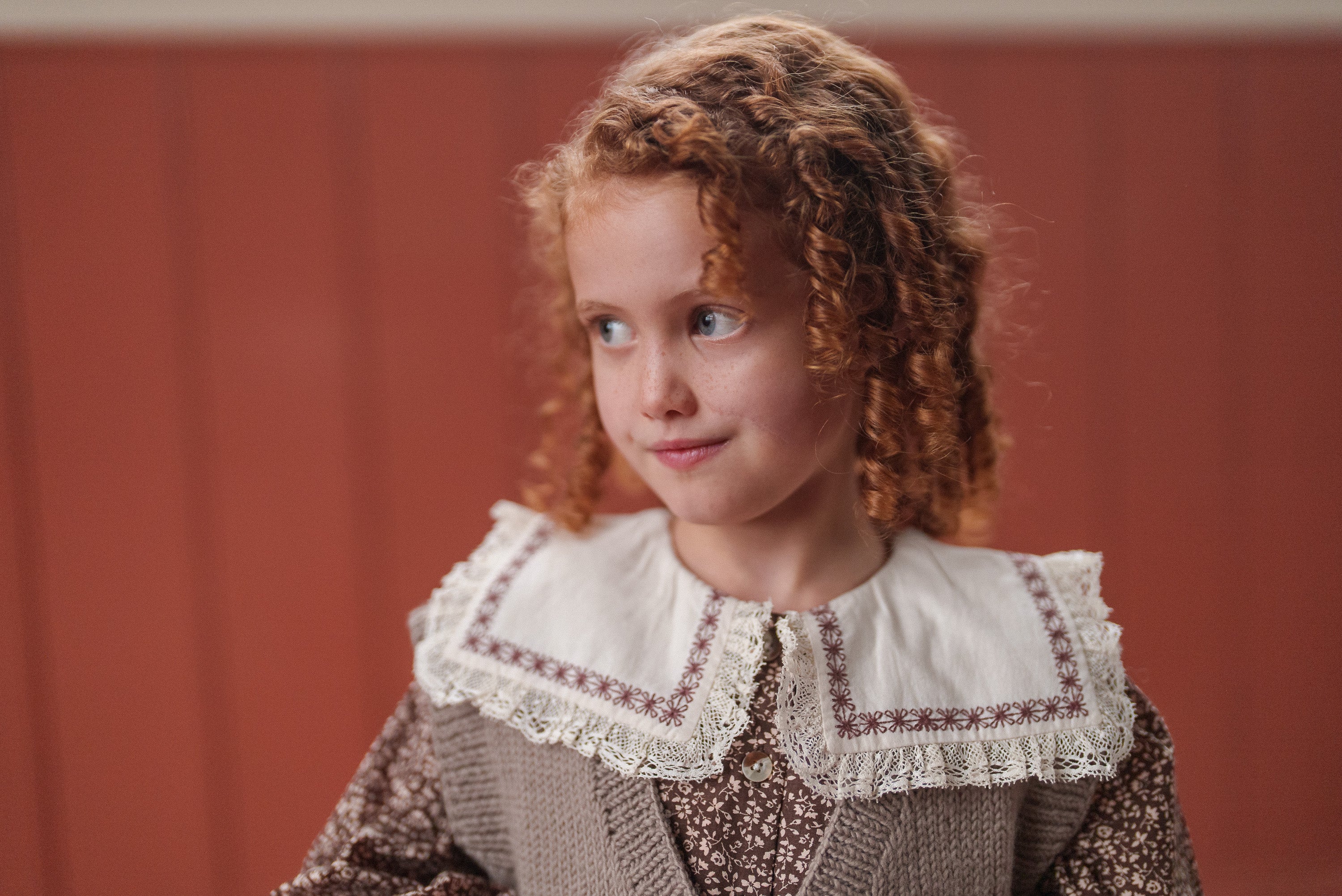 Young girl with curly hair wearing a vintage-style brown and beige floral blouse made from organic cotton, showcasing ethical and sustainable children's clothing.