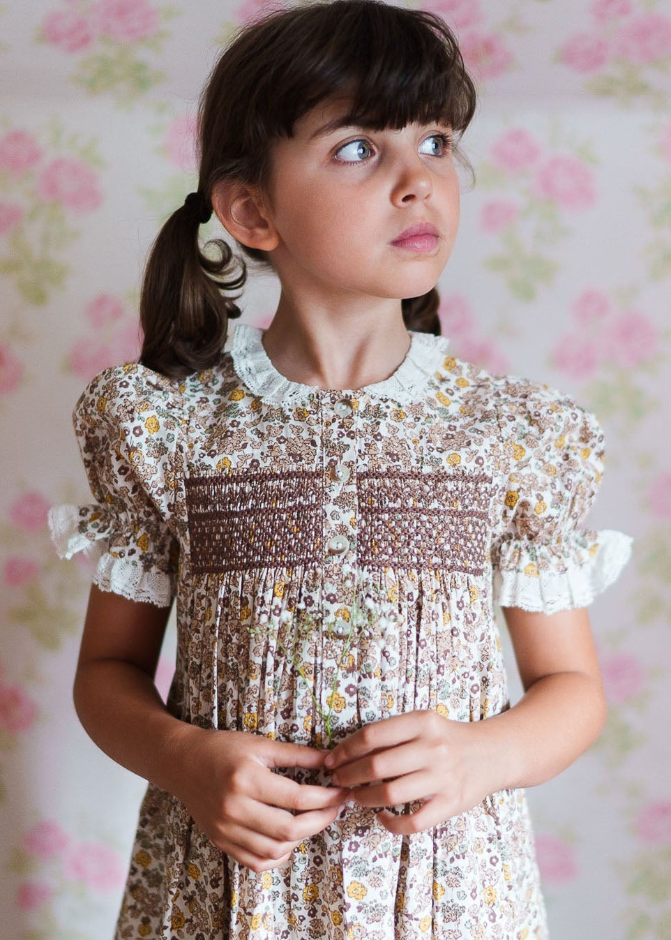 Young girl wearing a vintage style floral cotton blend dress with smocked detailing and puff sleeves, showcasing ethically made children's clothing in soft natural tones.