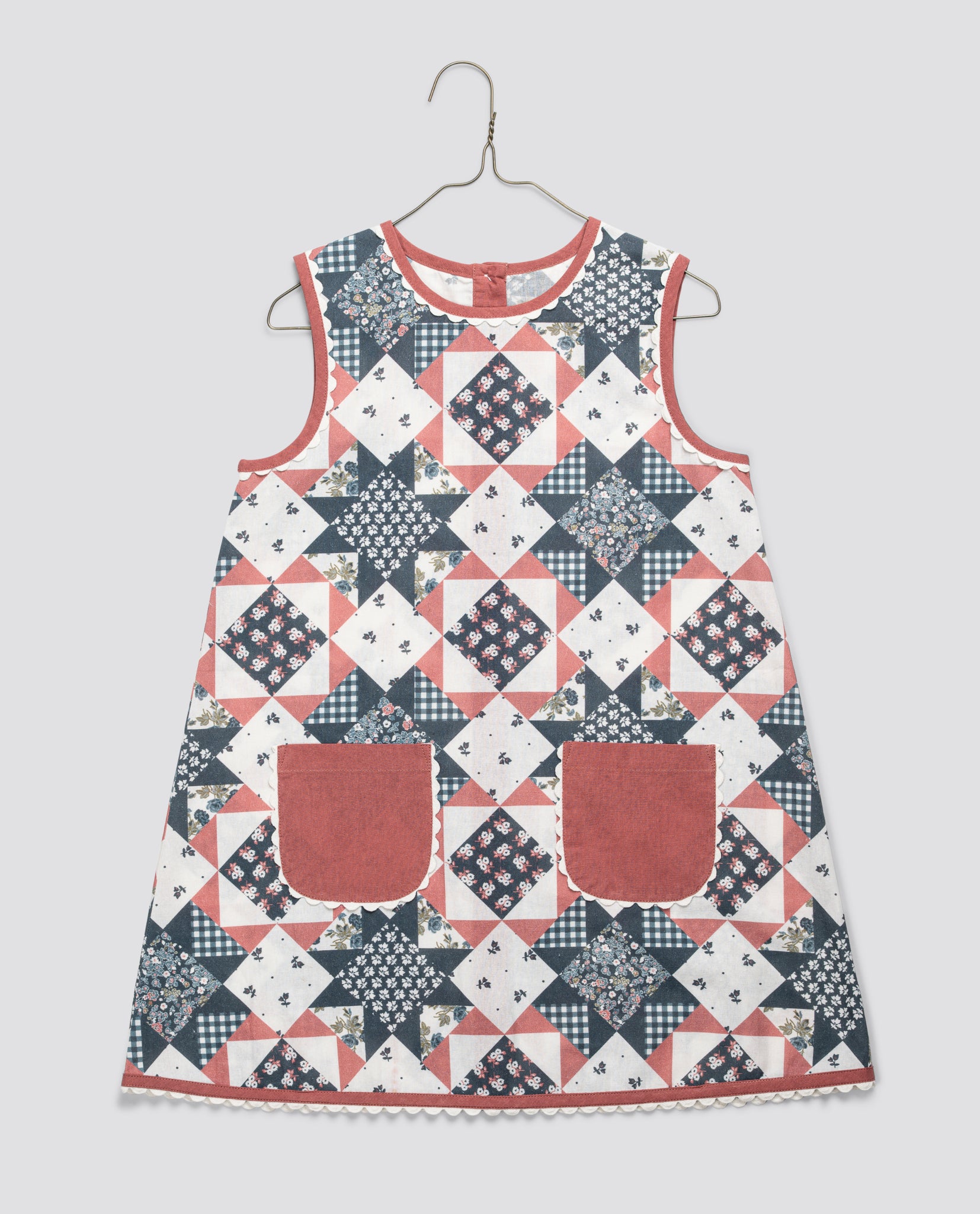 Sleeveless girls dress in a patchwork floral pattern with a cotton blend fabric, featuring vintage-inspired design and two front pockets in soft rose color, ethically made.