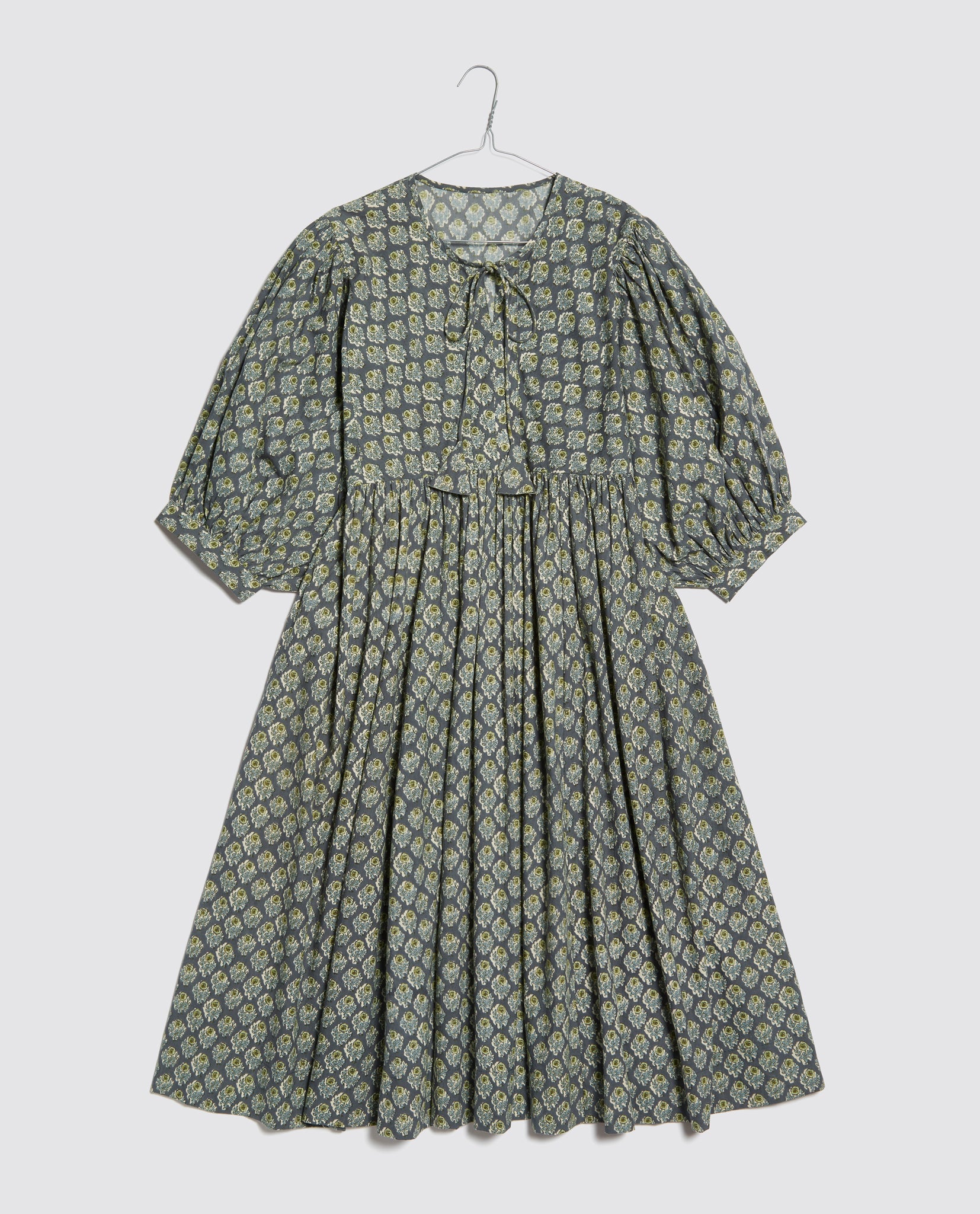 Vintage-inspired ladies dress in soft cotton with a delicate floral pattern, featuring puff sleeves and a tie neckline, made with organic, sustainable materials.