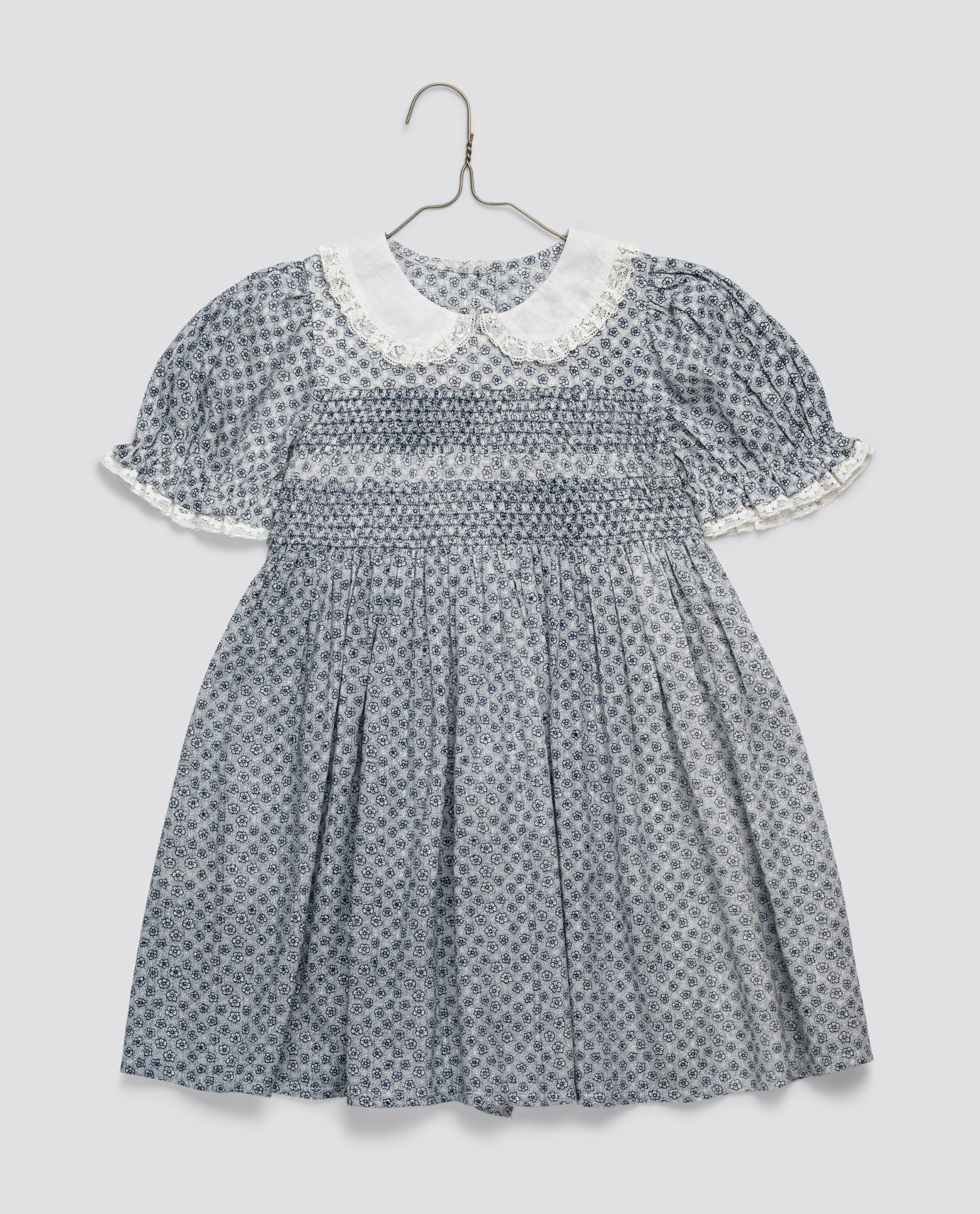 Blue floral vintage-style smocked girls dress with a white lace-trimmed collar and puff sleeves, made from a soft cotton blend for gentle, sustainable children’s clothing.