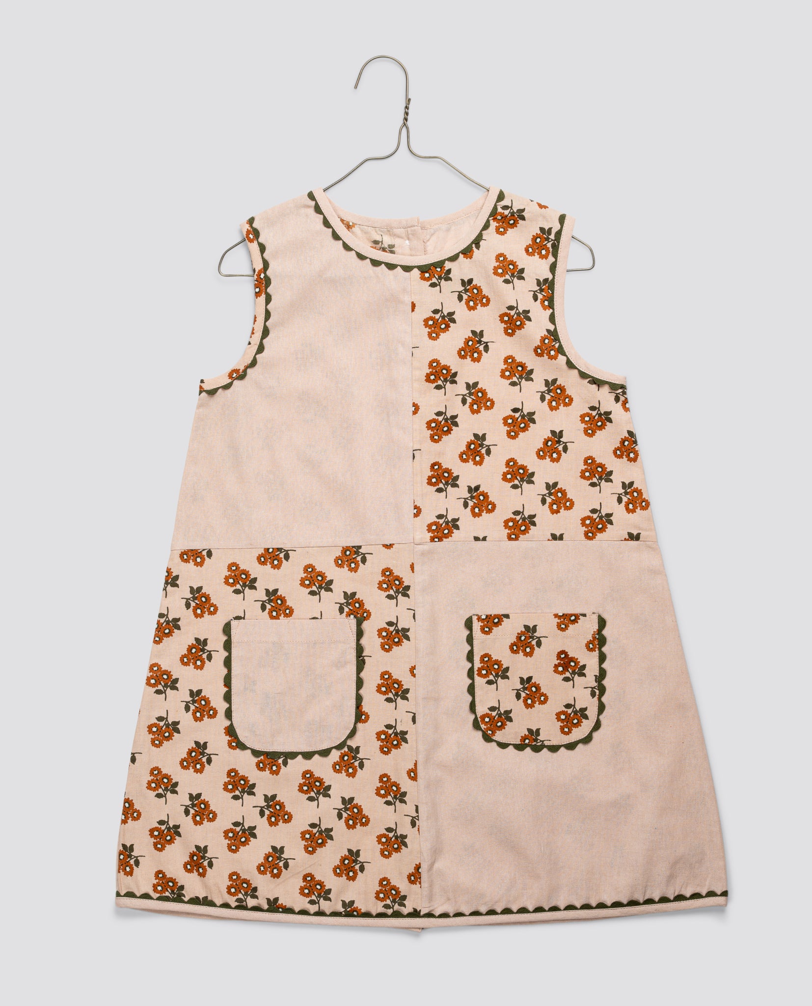 Vintage style sleeveless girls dress made from organic cotton with a marigold floral pattern and decorative pockets, reflecting natural and sustainable children’s clothing.