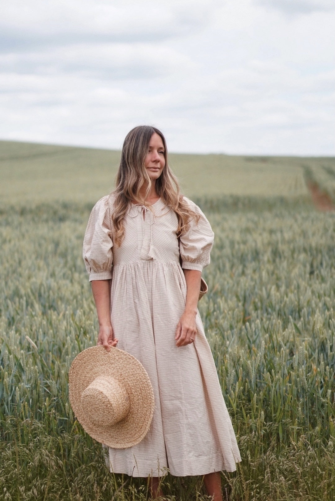 Woman in a beige dress holding a straw hat in a field