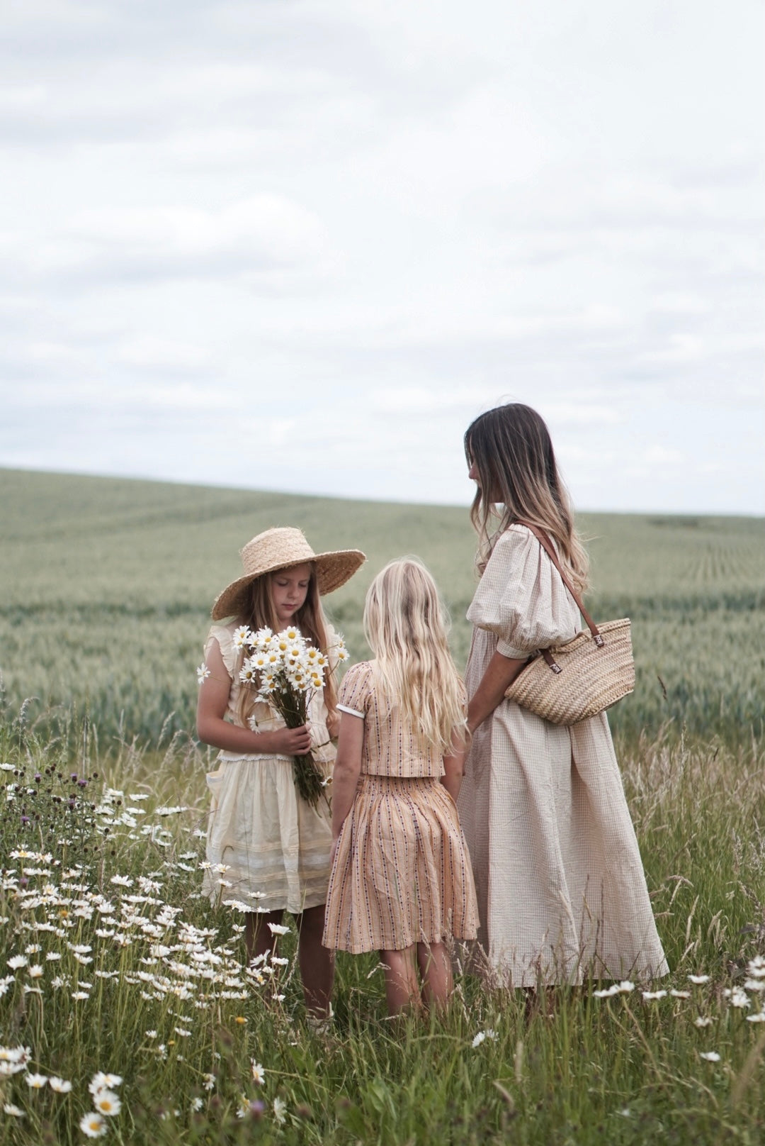 Three women in dresses standing in a field with flowers
