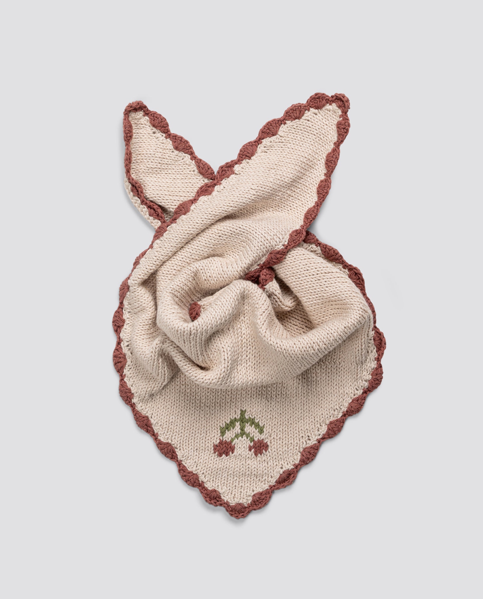 Soft cream cotton scarf with hand-knitted cherry detail and vintage-inspired rust-colored scalloped edges, crafted sustainably for children’s organic clothing.