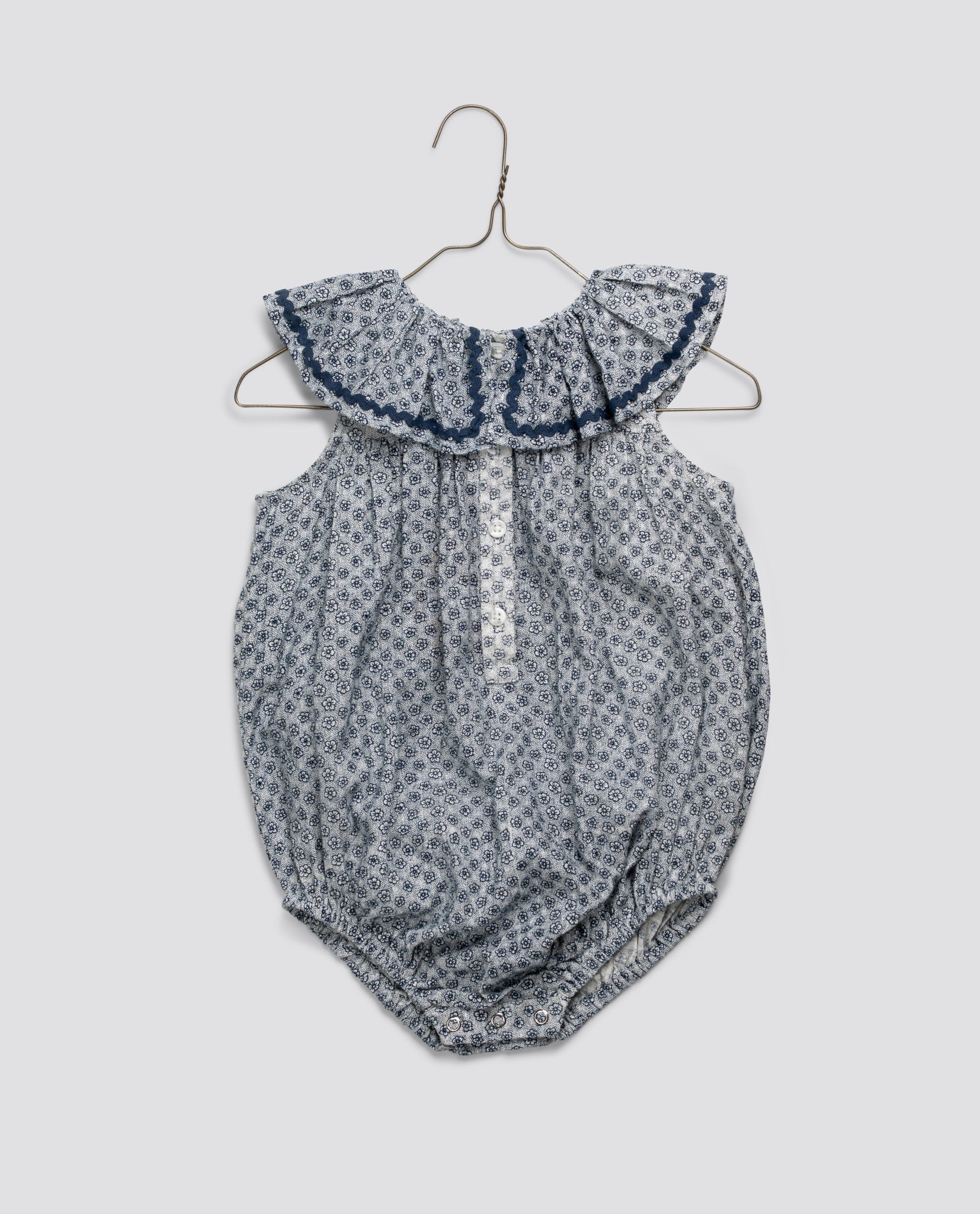 Vintage-style baby romper in soft organic cotton featuring a delicate floral pattern and ruffled collar, designed with sustainable, ethical craftsmanship.