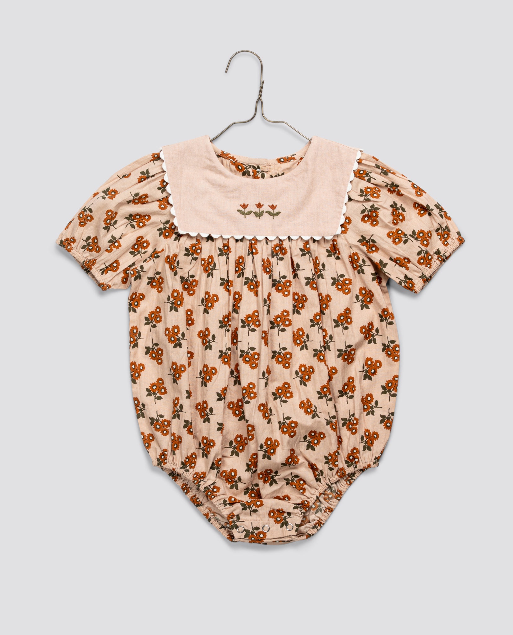 Soft organic cotton baby romper in marigold floral print with vintage-inspired embroidered yoke and puffed sleeves, designed with sustainable, ethical craftsmanship.