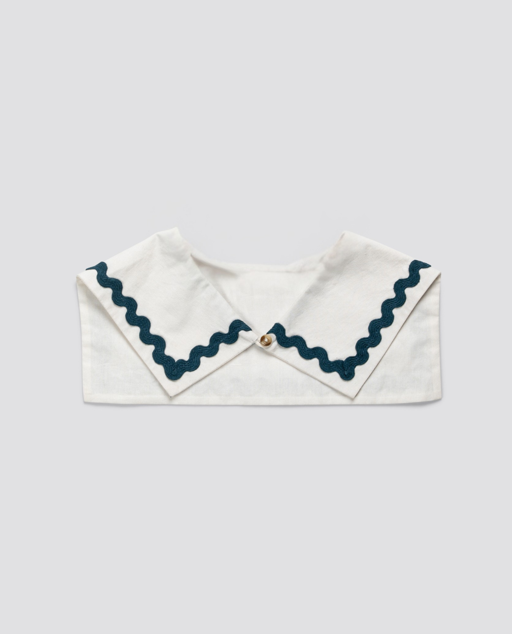 White organic cotton sailor-style collar with navy blue rickrack trim and a small button detail, reflecting vintage-inspired sustainable children's clothing.