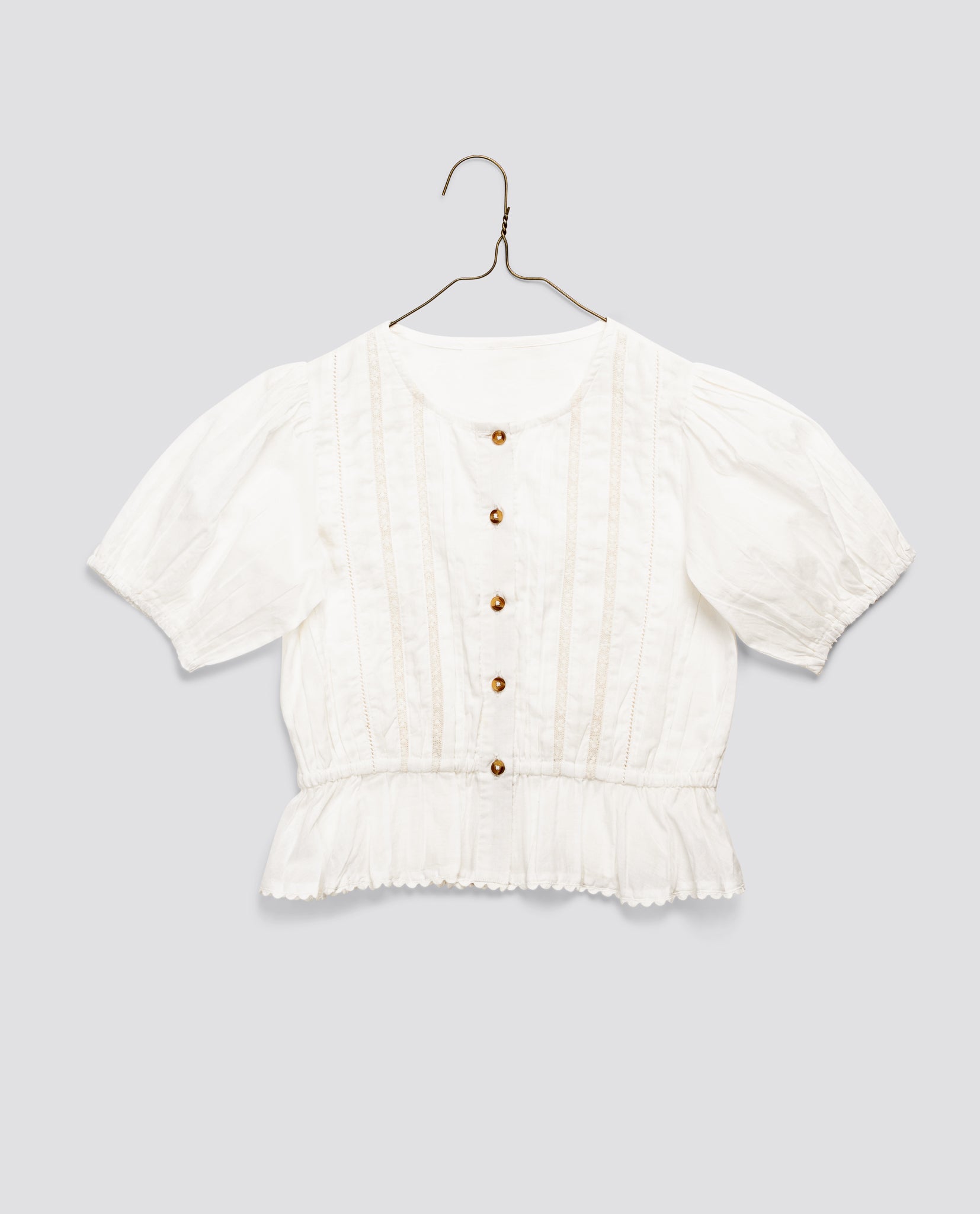 Off-white organic cotton blouse for girls with vintage-inspired details, short puffed sleeves, delicate buttons, and a gathered hem, made sustainably and ethically.