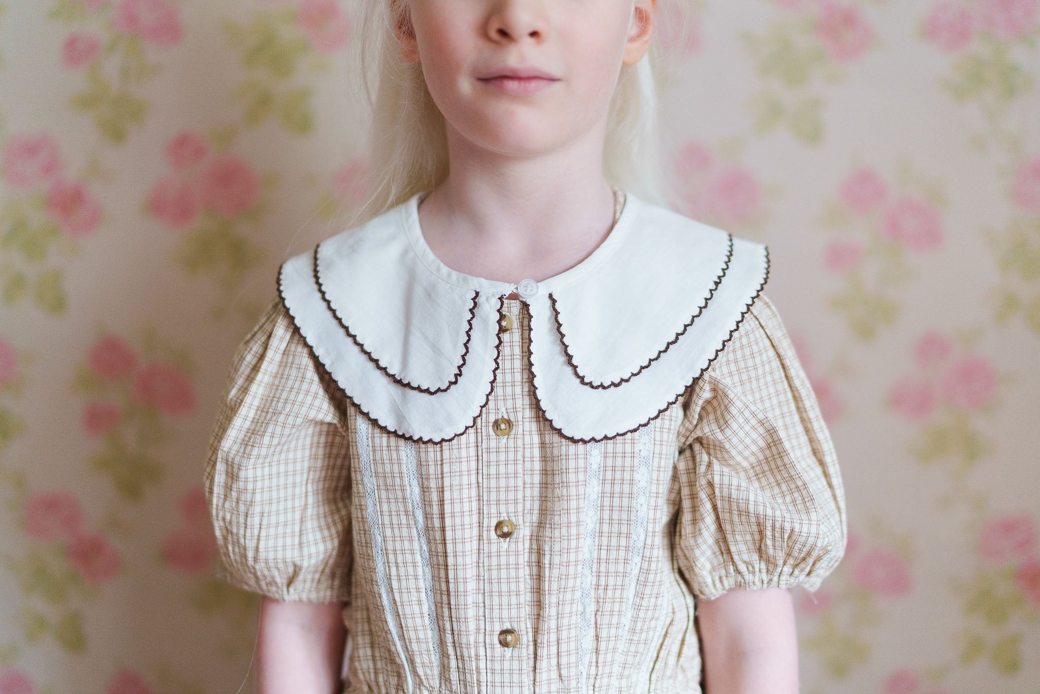 Young girl wearing a vintage style dress with a natural organic cotton double layer collar, featuring puffed sleeves and a delicate check pattern in a soft, sustainable fabric.