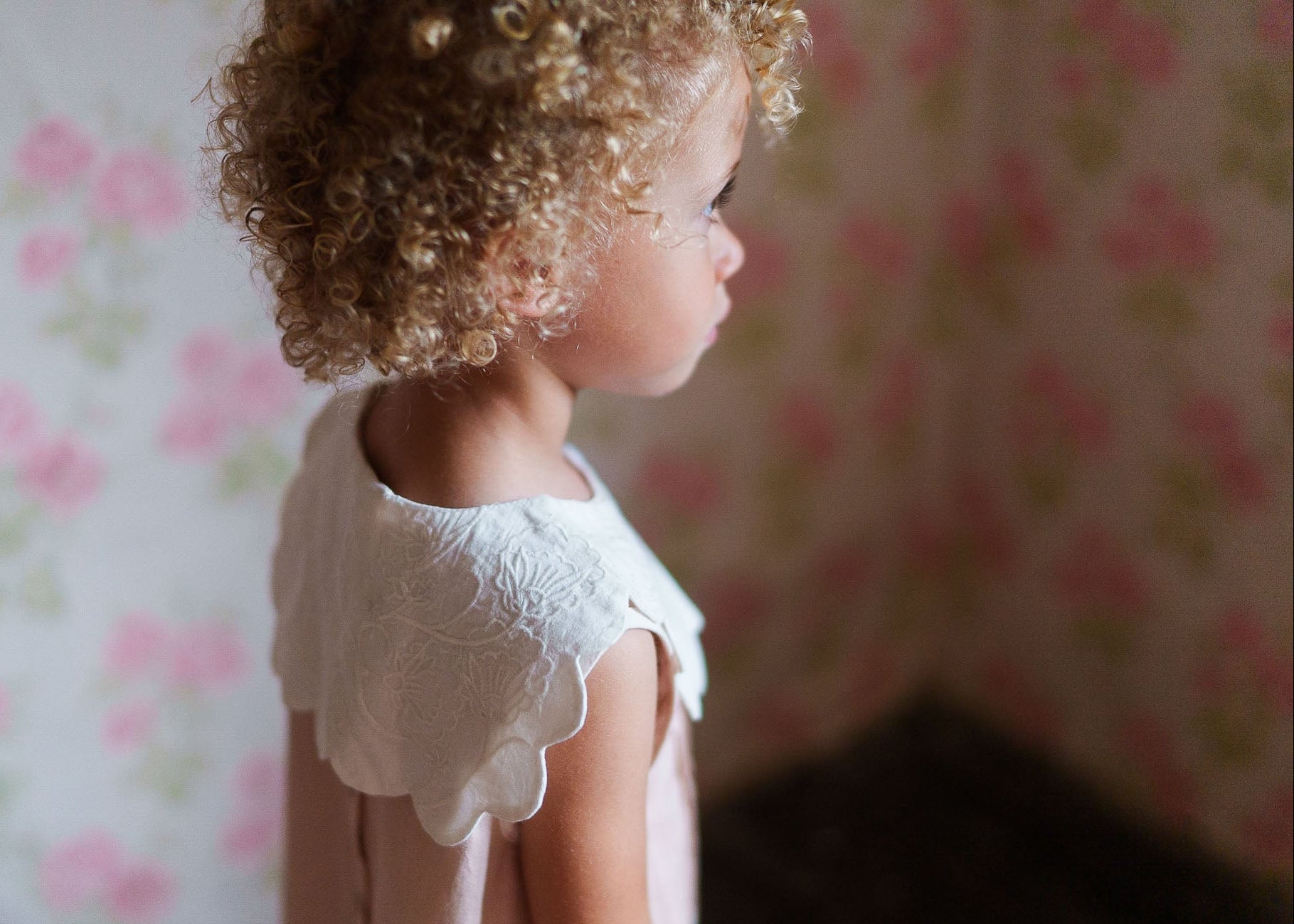 Young child wearing a vintage style dress with an organic cotton embroidered scalloped collar, highlighting sustainable, ethically made children's clothing in a soft, natural setting.