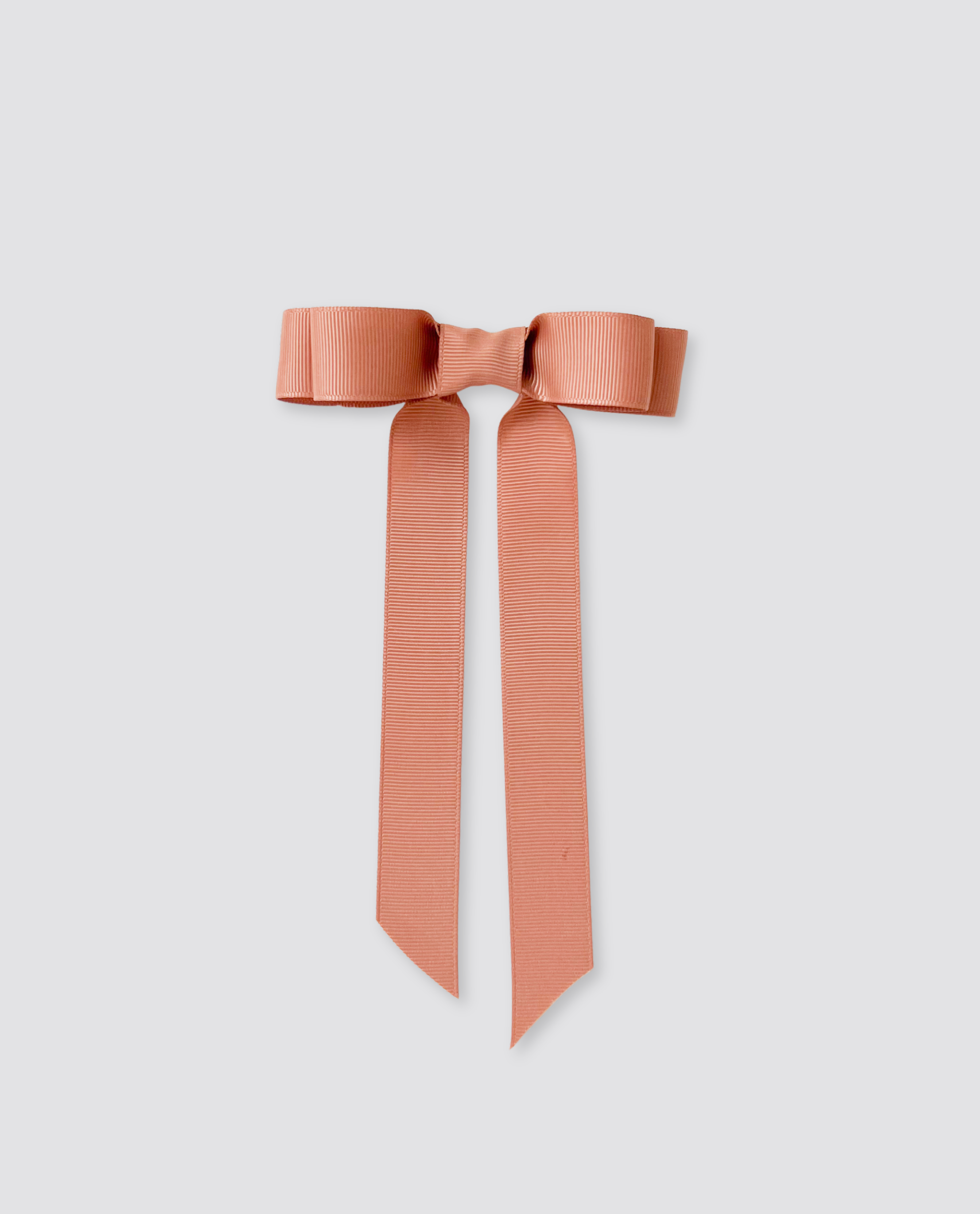 Salmon-colored grosgrain hair bow with long tails, designed for children, reflecting a vintage style with a natural and ethical approach to kids' accessories.