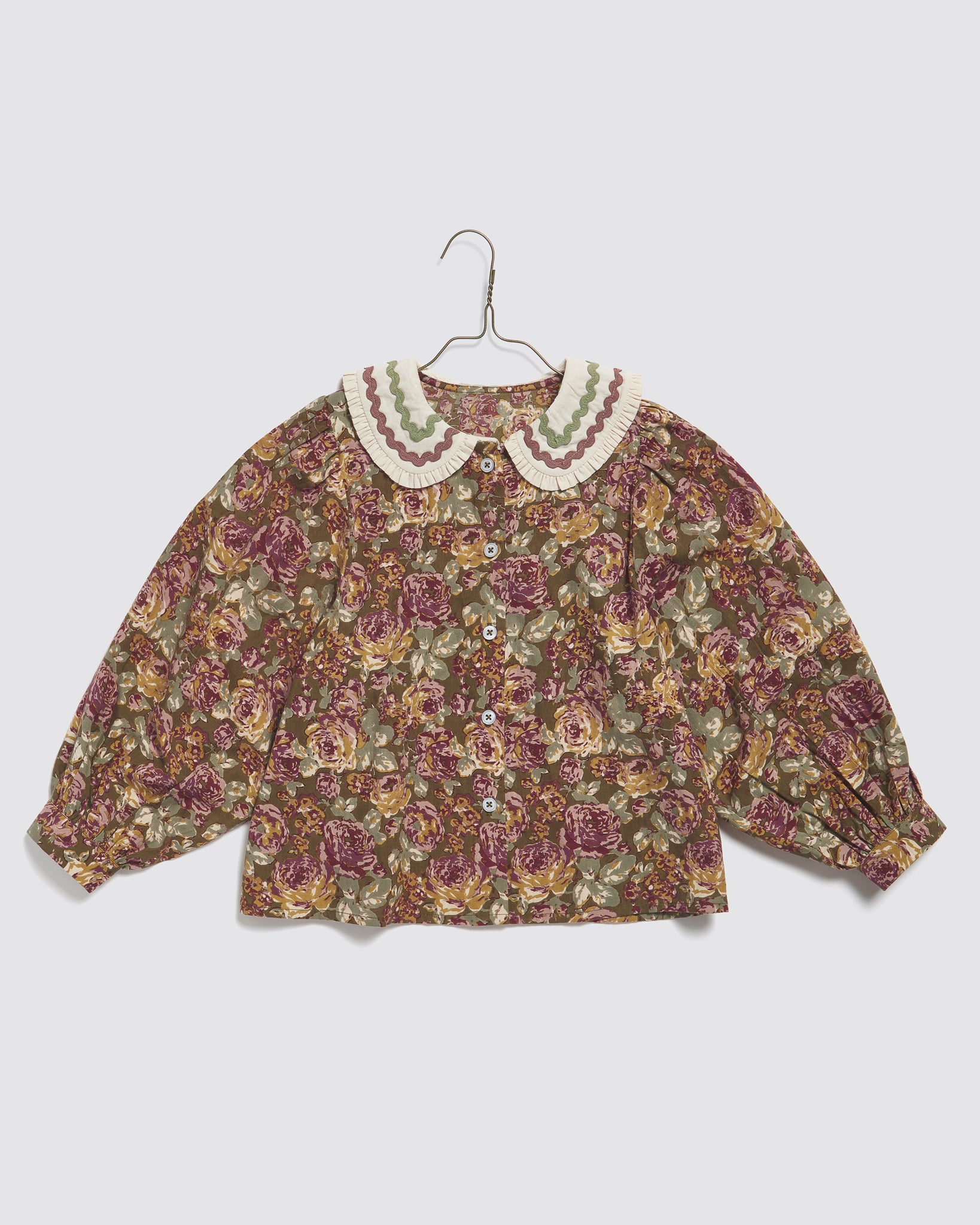 Girls vintage-style blouse in organic cotton featuring a floral pattern with green and pink tones, a playful Peter Pan collar, and ric-rac trim, ethically made for kids.
