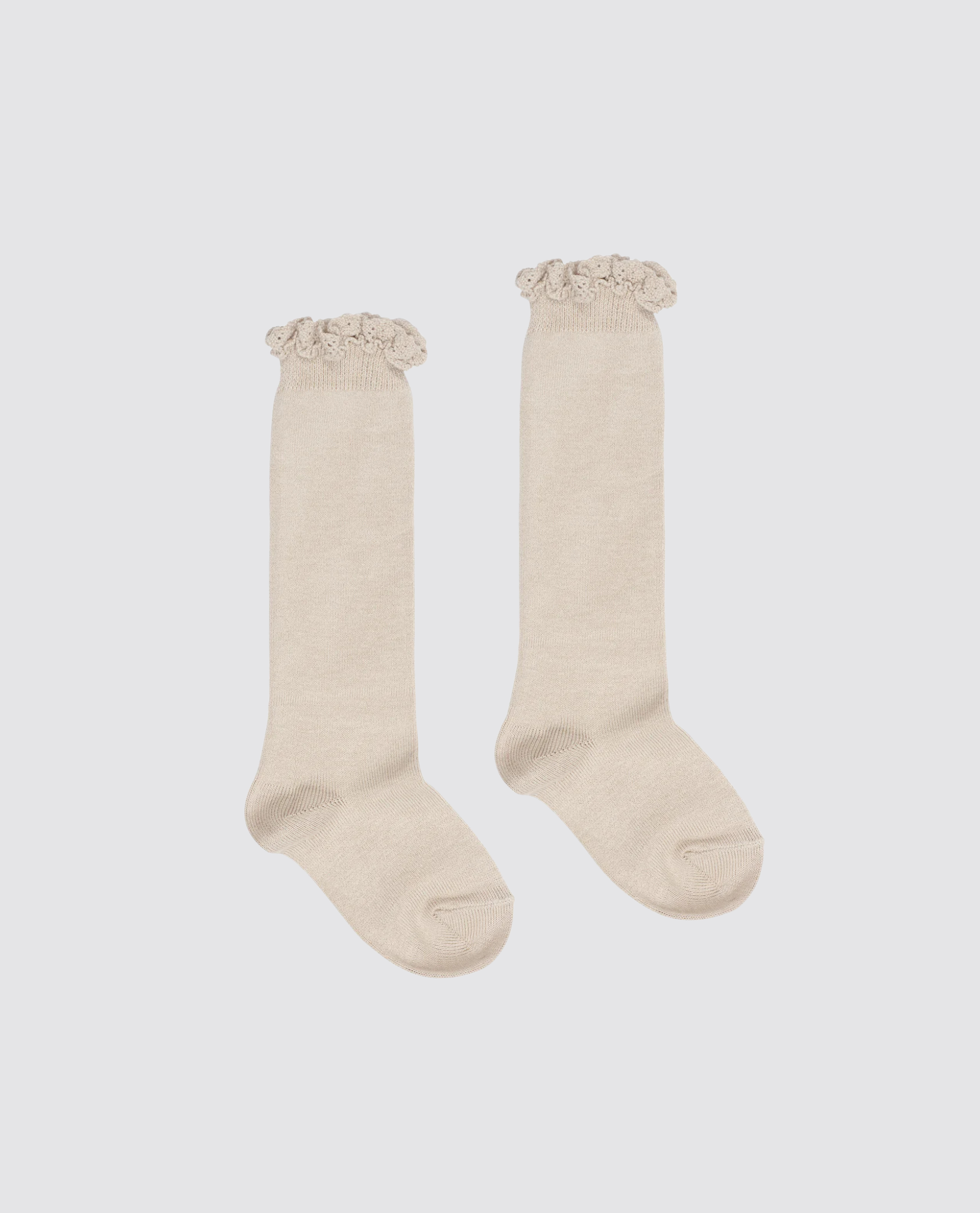 Pair of beige knee-high socks for kids with delicate lace frill trim, made from a soft cotton blend, reflecting vintage-inspired, sustainable children's clothing.