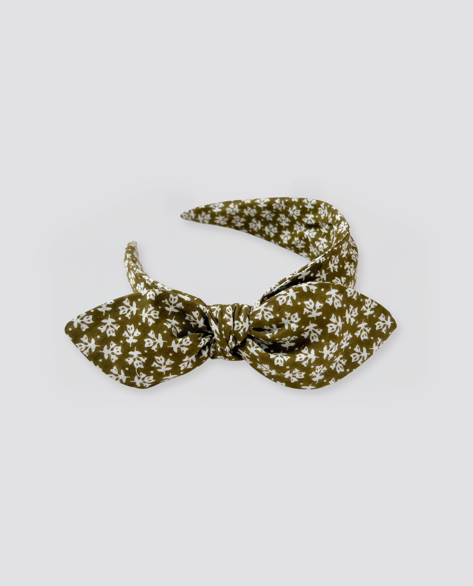 Wide retro-style hairband for children in a soft olive green fabric with a delicate white floral pattern, crafted with natural, sustainable materials for gentle everyday wear.