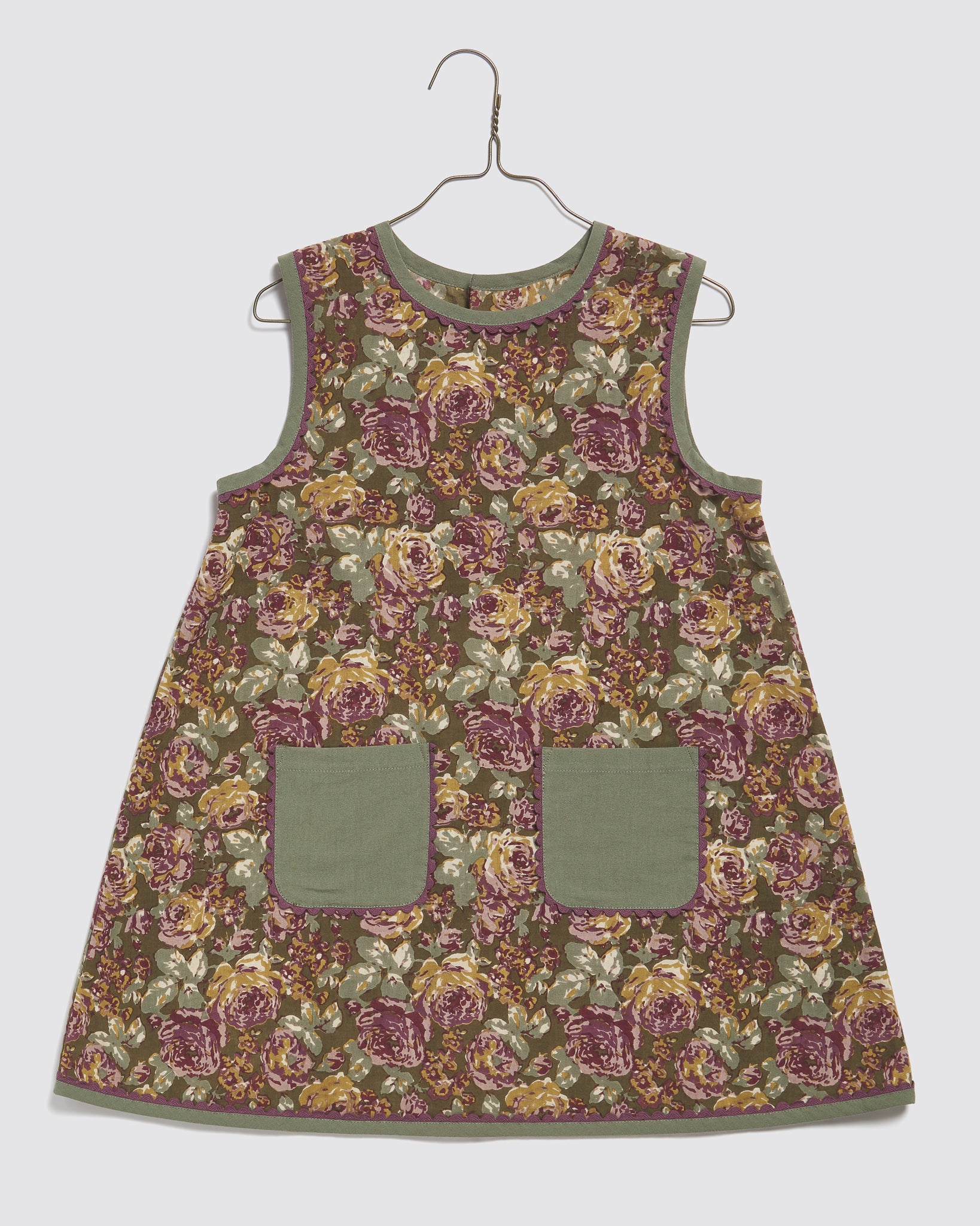 Vintage style sleeveless girls dress made from organic cotton fabric with a green floral pattern and two solid green front pockets, designed for sustainable kids clothing.