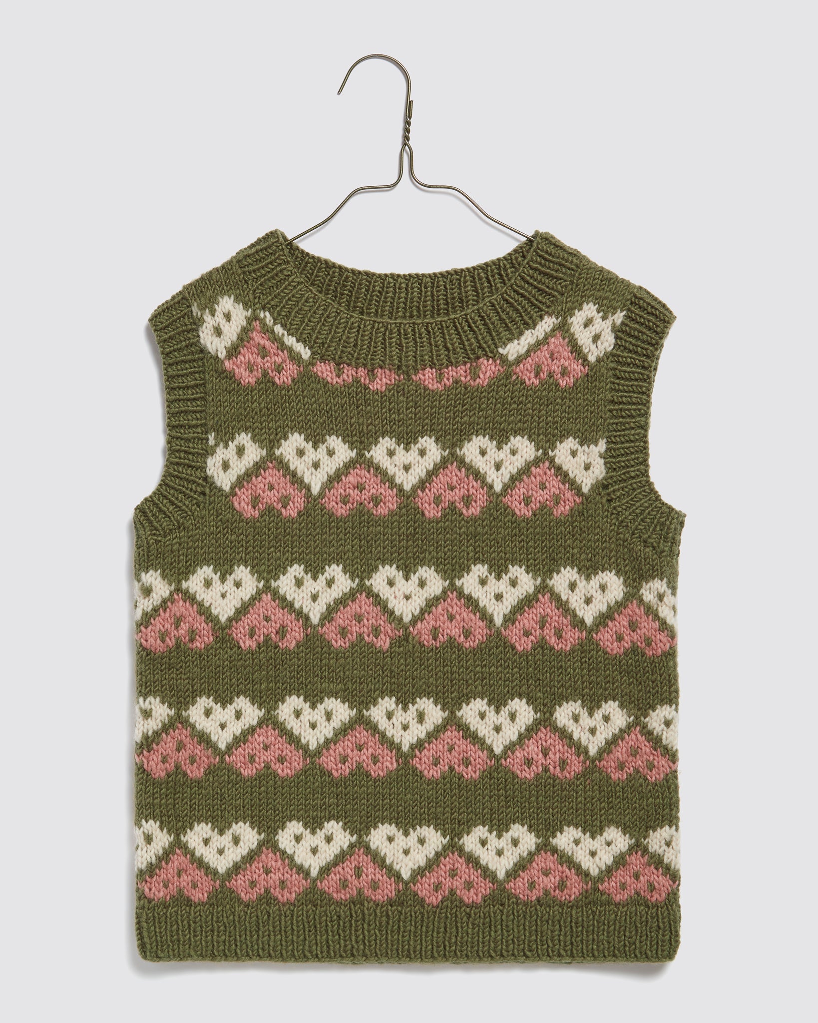 Hand-knitted green merino vest for kids with a vintage-inspired heart pattern in cream and pink, made from organic, sustainable materials for ethical children's clothing.