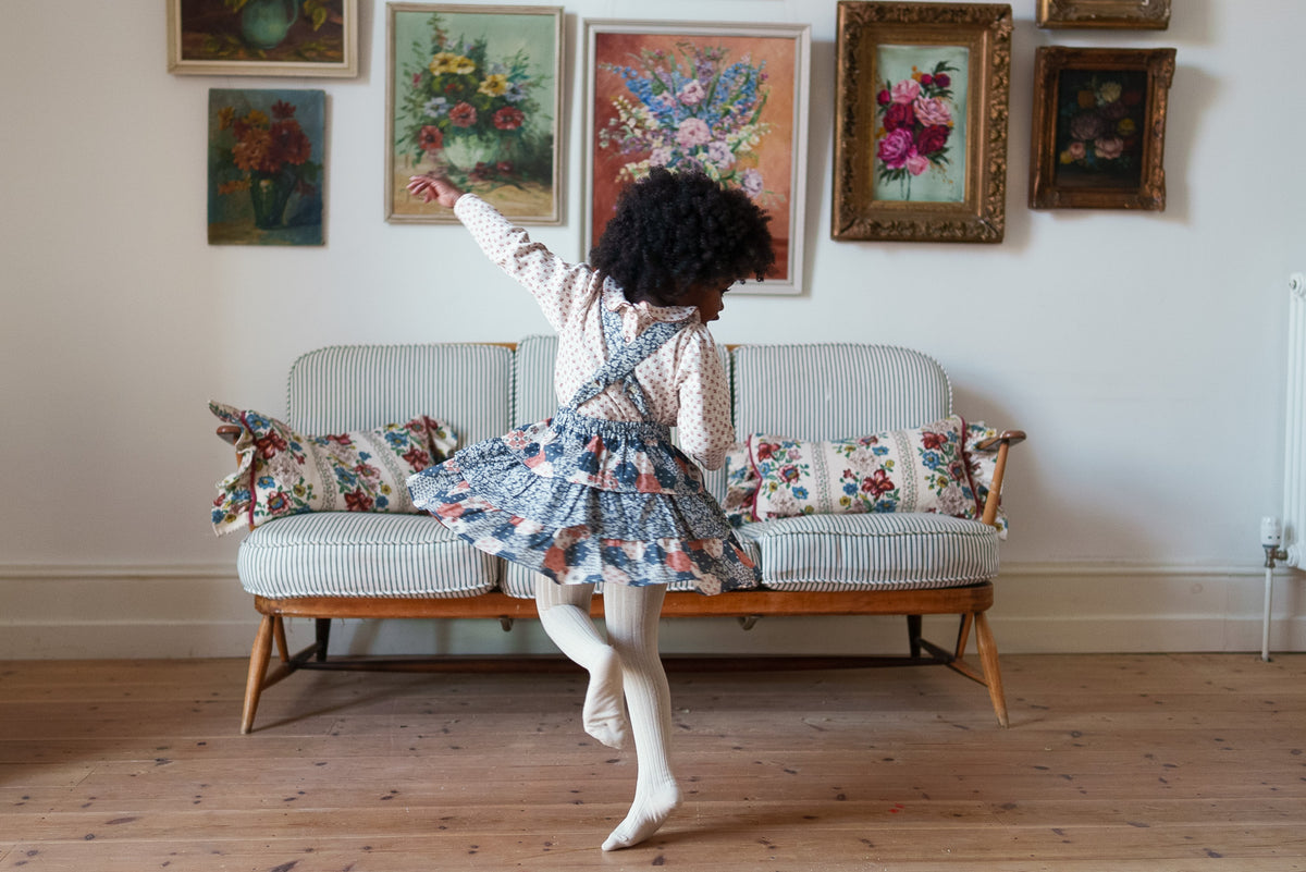 Young girl wearing patchwork floral Rara skirt, twirling in front of striped sofa with classic flower paintings on the wall, showing sustainable and vintage-inspired values.