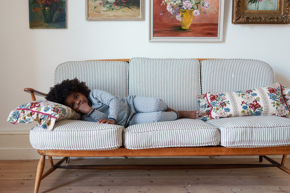 Child wearing white and black floral cotton pointelle pyjama set laying on striped sofa with head against colourful floral pillow.