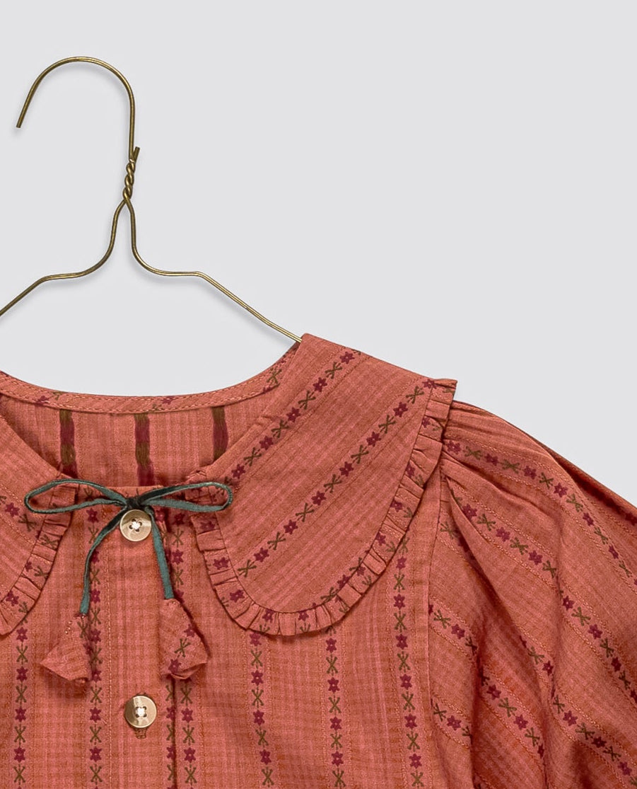 A terracotta-colored long-sleeve blouse with vertical black stripes, a Peter Pan collar, and a front button closure, hanging on a metal hanger against a light gray background.