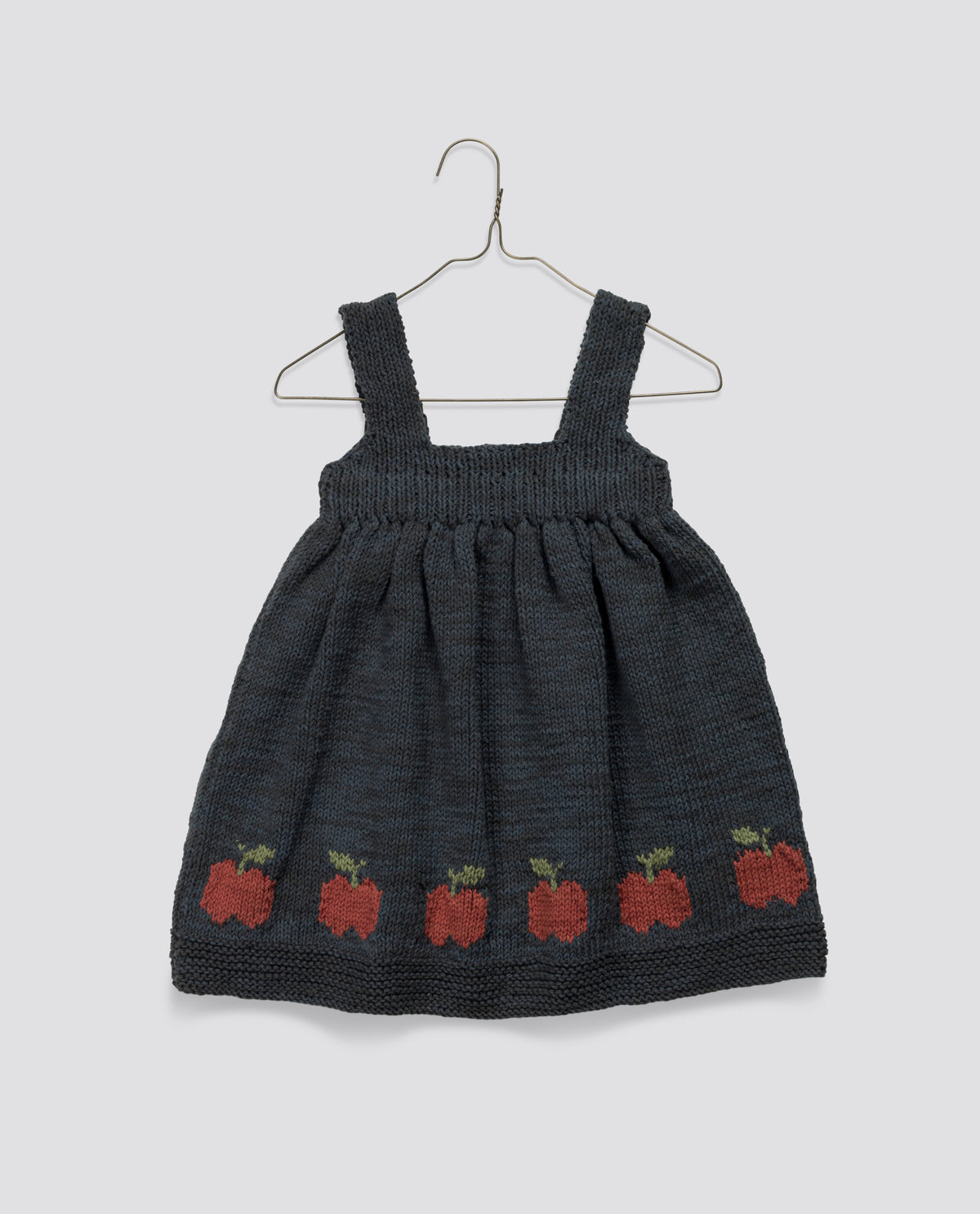 Hand knitted navy and red pinafore dress for children made from soft materials featuring a vintage-inspired apples pattern along the hem, crafted sustainably.