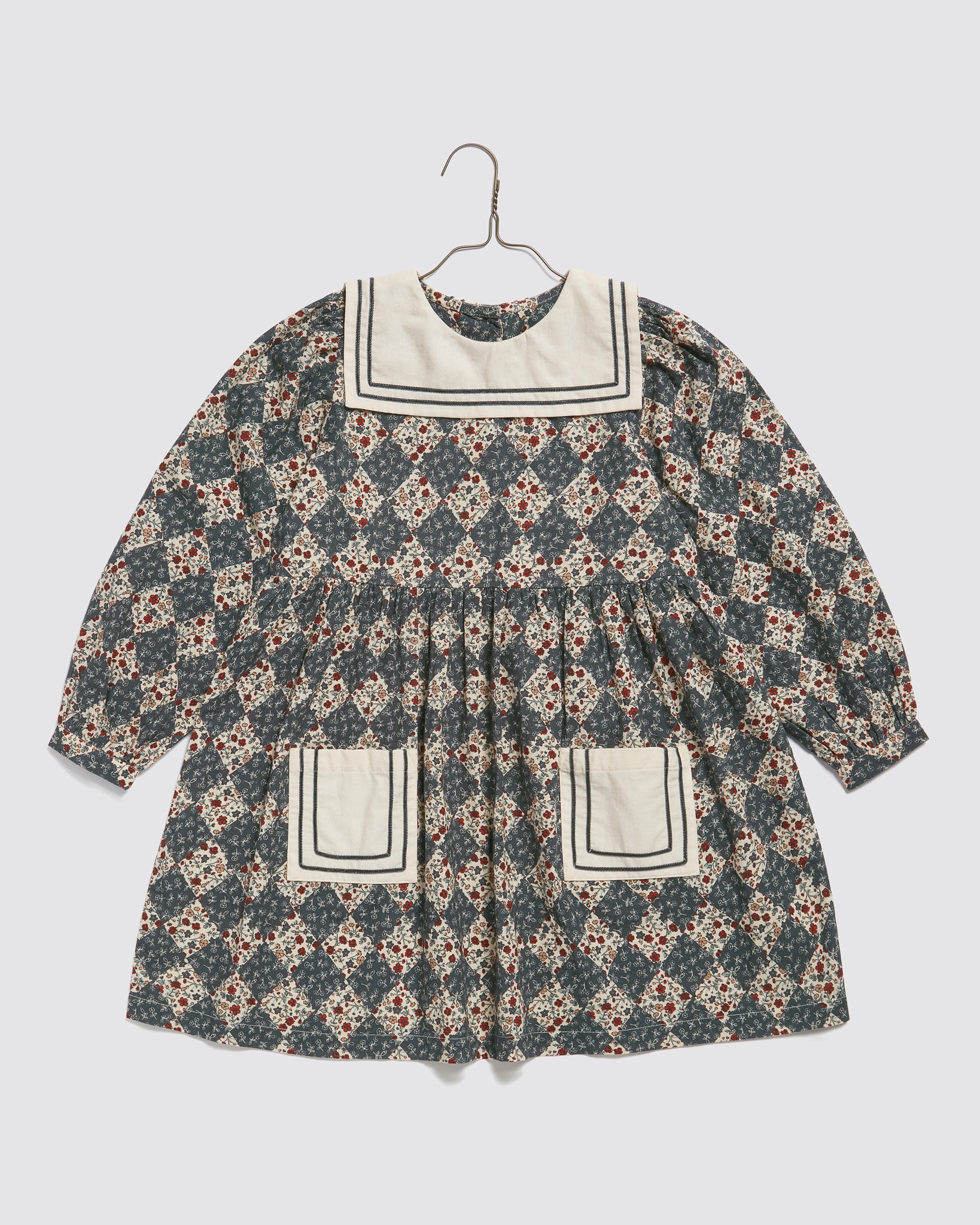 Vintage style girls dress made from organic cotton with a navy floral harlequin pattern, featuring a sailor collar and front pockets, designed for sustainable children's clothing.