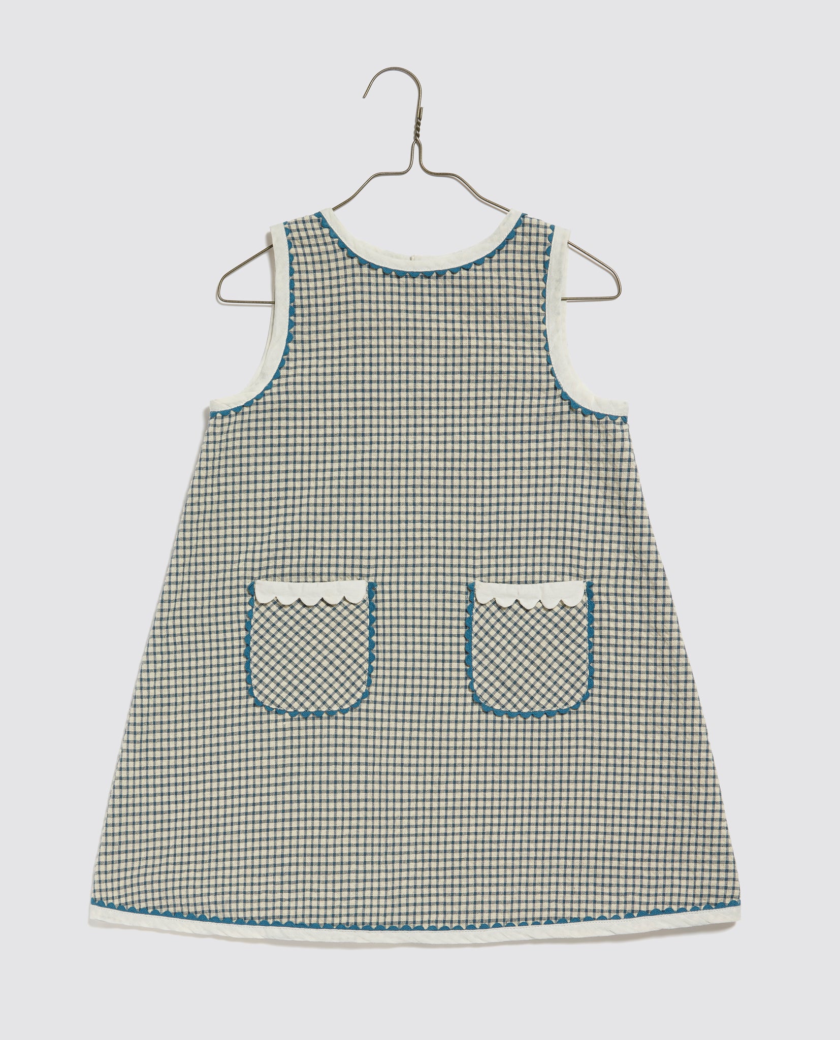 Vintage style sleeveless girls' dress in navy and white checkered organic cotton with scalloped trim on pockets, designed sustainably and ethically for childhood.