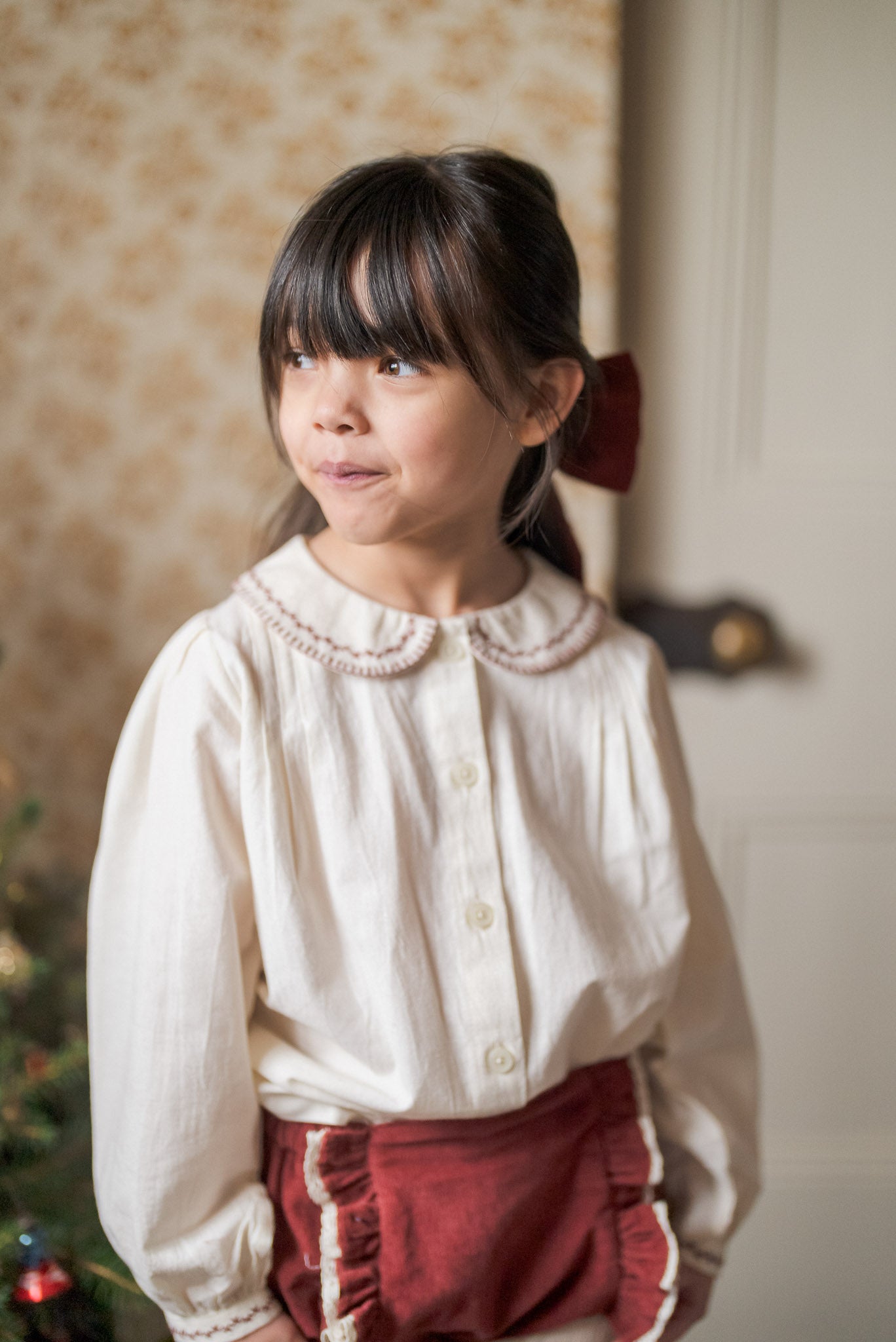 Young girl wearing vintage style children's clothing with a white organic cotton blouse and red velvet bow clip, showcasing natural, ethical, sustainable kids fashion.