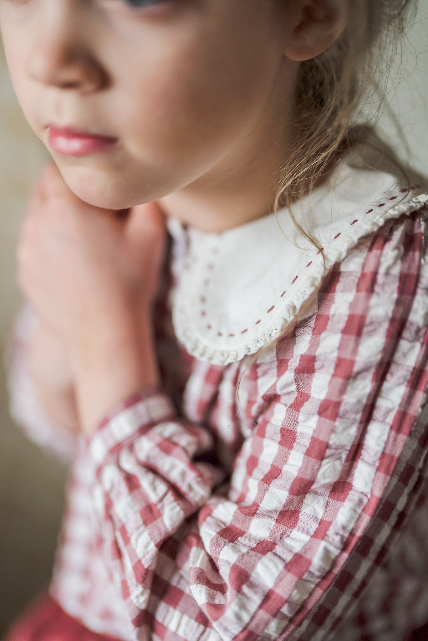 Close-up of a young girl wearing a soft cotton gingham blouse in white and red checks with a vintage-style embroidered collar, showcasing sustainable children's clothing.