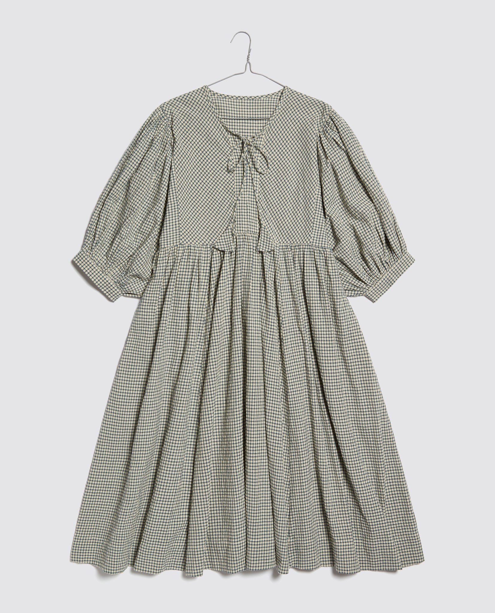 Rustic check vintage-style ladies dress made from organic cotton with puffed sleeves and a front tie, reflecting a slow, natural, and ethical design ethos.