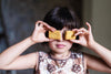 Model holds custard cream biscuits in front of her faec whilst wearing a patchwork print dress with ric-rac trim.