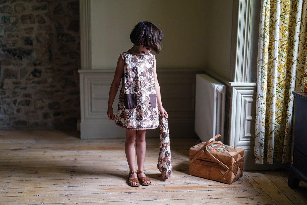 Vintage style A-line girl's dress in printed patchwork design fabric. Short length summer dress, sleeveless with pockets with ric-rac trim. 