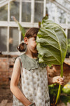 Model hides behind large leaf whilst wearing a pretty, scalloped sailor collar and vintage inspired, sleeveless summer dress. 