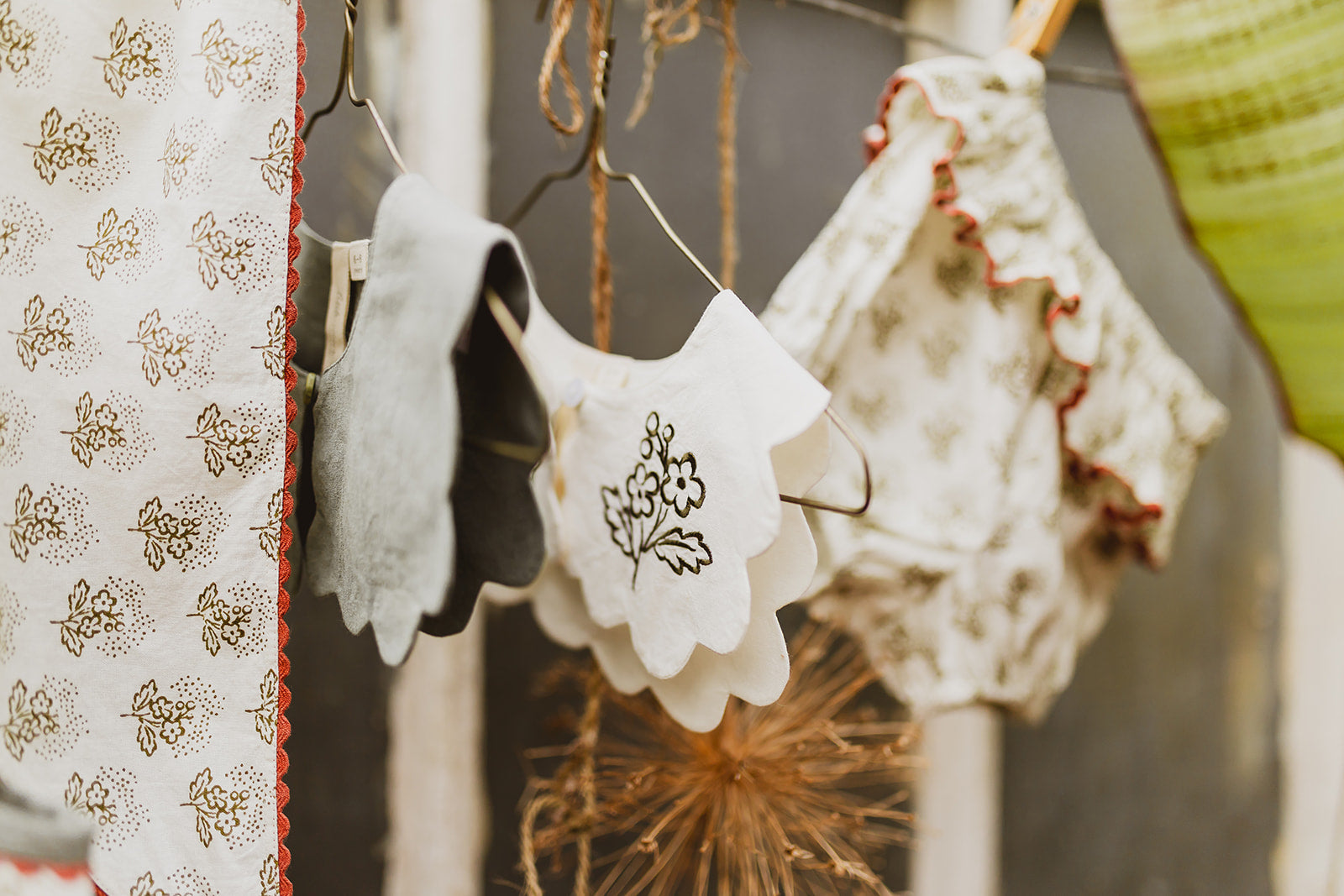 Vintage style scalloped collars and organic cotton baby clothing hanging on a line, showcasing natural, ethically made children's apparel with delicate floral details.